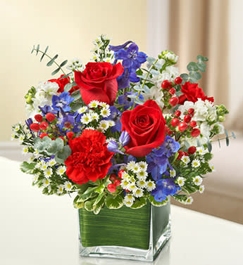 Healing Tears - Red, White and Blue - This lovely red, white and blue sympathy arrangement offers a beautiful reflection of your patriotism, sympathy and support. Fresh red roses, delphinium, stock, carnations and hypericum, designed in a cube vase, provide a stunning tribute sent to the home or service. 