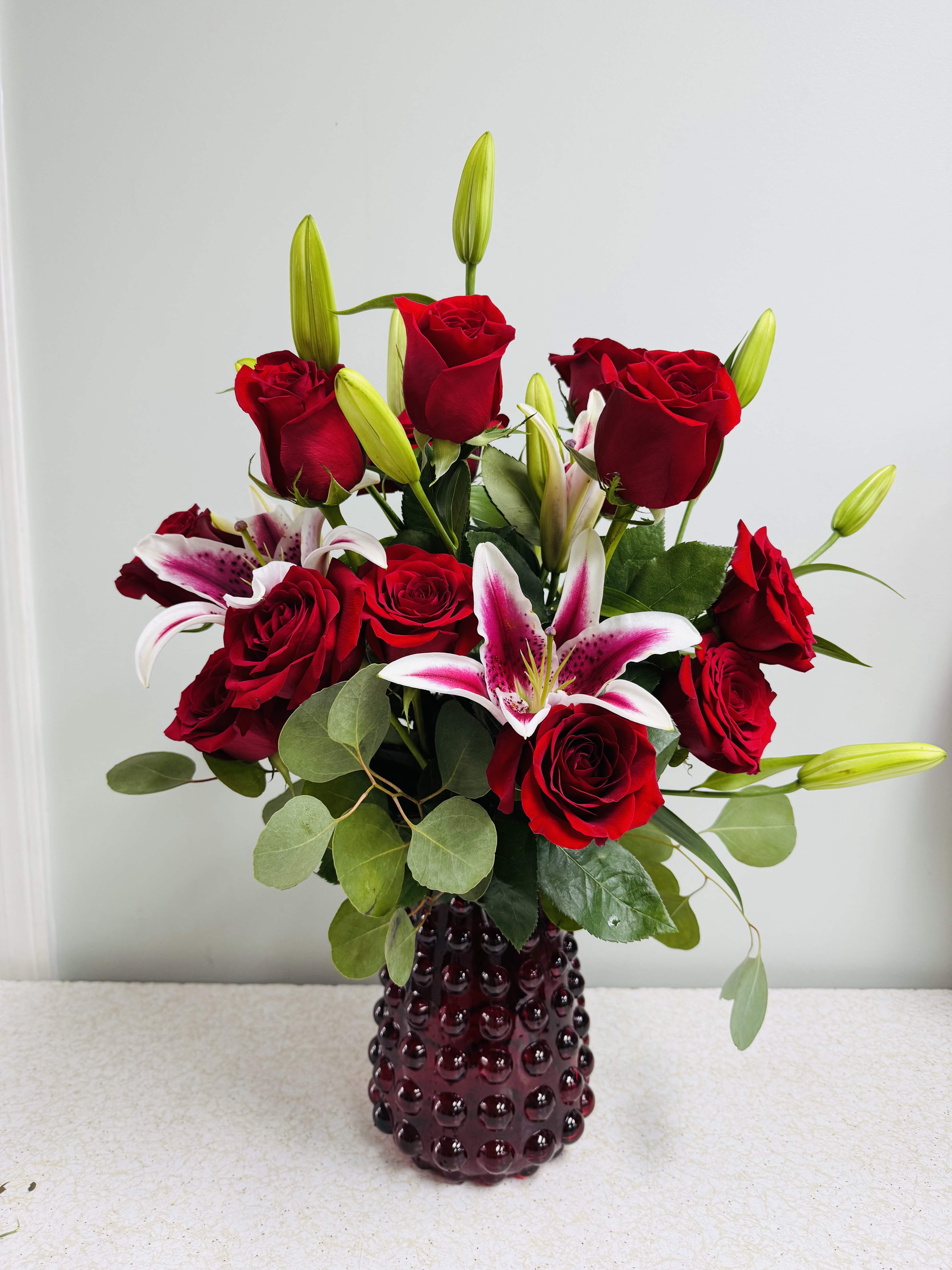 Always and Forever - This signature arrangement features a dozen roses, three star-gazer lillies, two types of greens, and filler. It's a real beauty and so fragrant! If only you could smell these through the website. In a clever red bubble vase while supplies last!