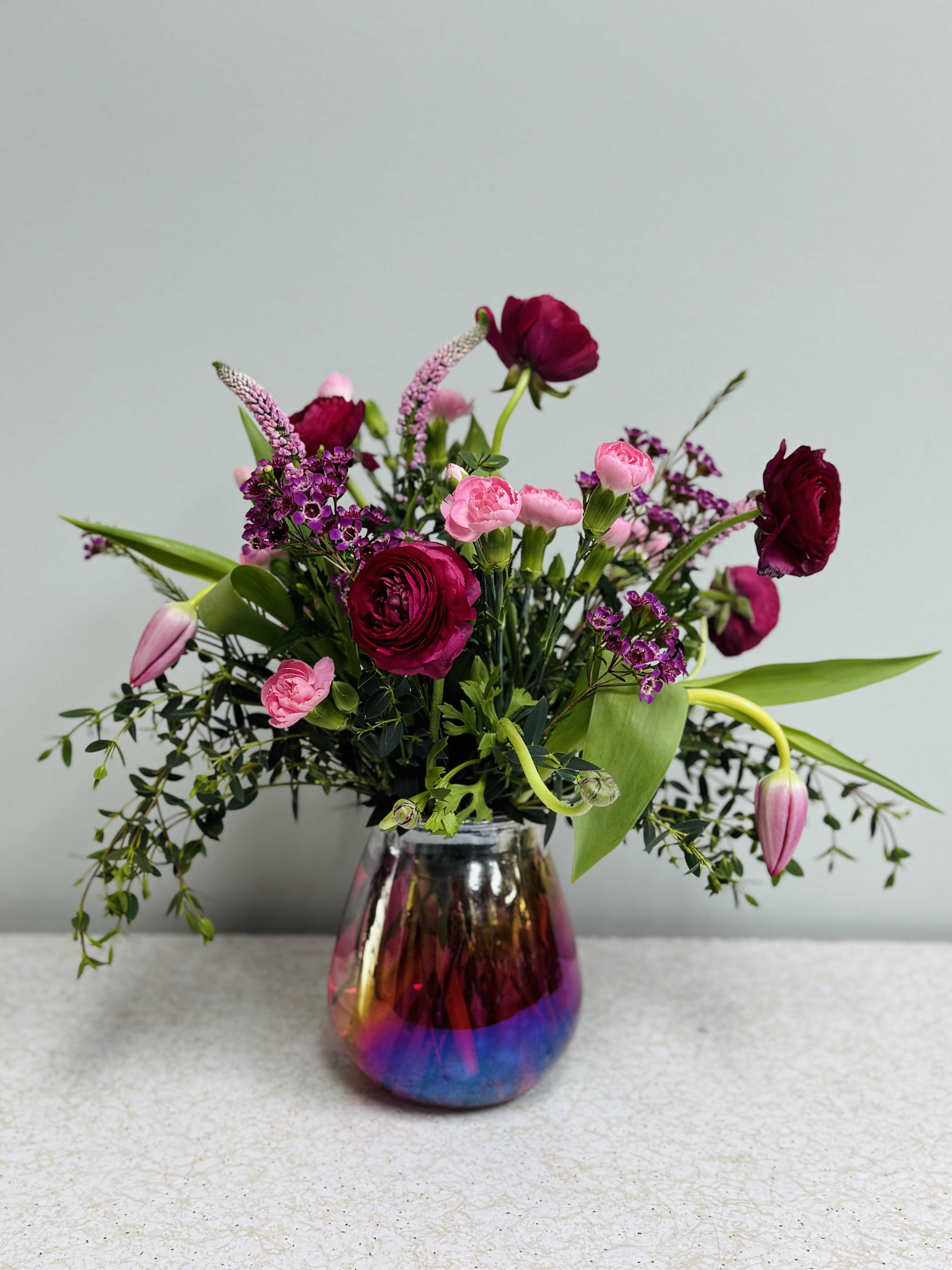 P.S. I Love You - This sweet little bouquet packs a big style punch! With a pink ombre-iridescent vase, its full of eucalyptus, ranunculus, tulips, wax flower, and filler. It's a real show-stopper! 