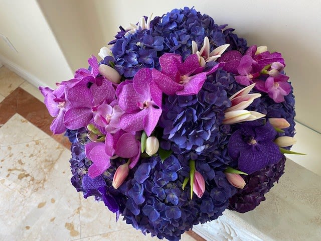Stormy Blue Centerpiece - A mix of premium flowers with Hydrangas, Orchids and Tulips arranged round in a low ceramic container.