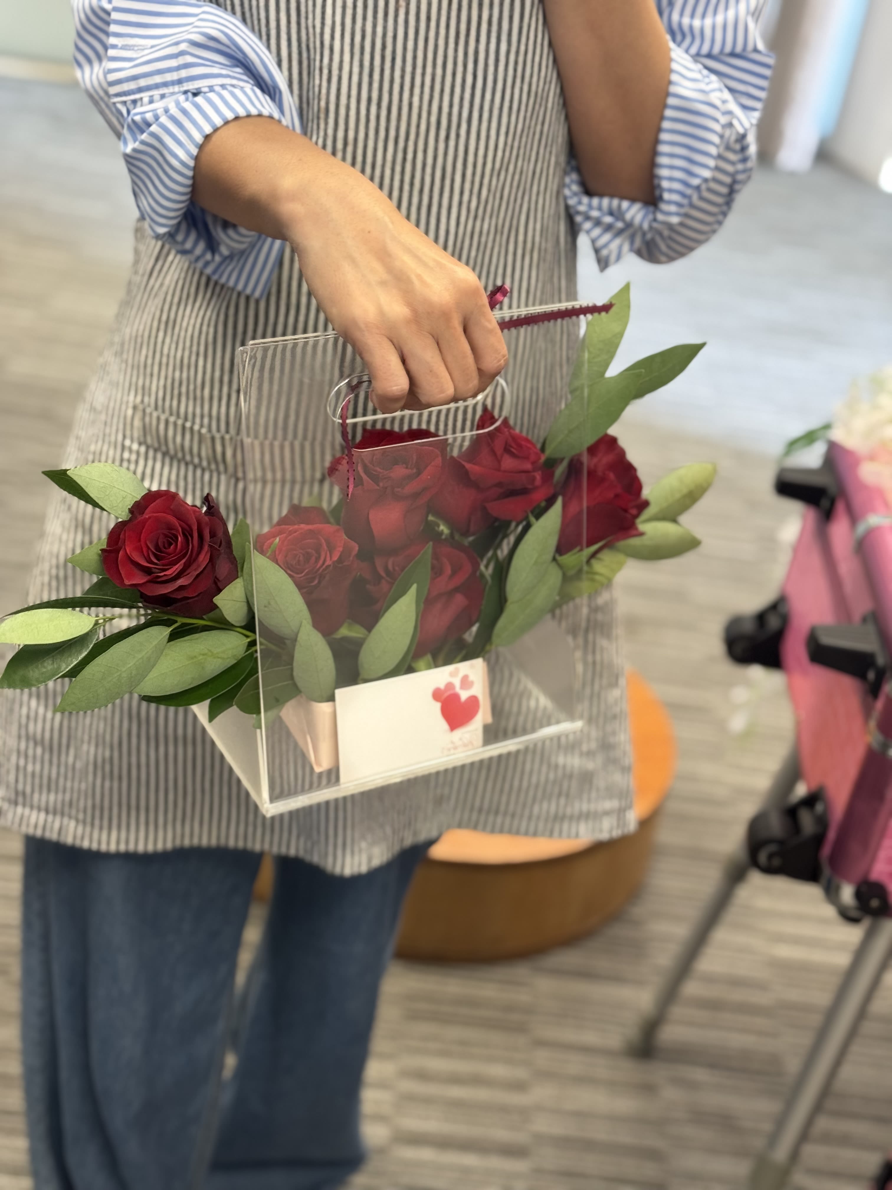 Classic Handheld Bloom Box - A charming and modern rose arrangement featuring fresh deep red roses nestled with lush greenery in a clear handled gift box. Designed for easy carrying and instant gifting, this bloom box blends elegance with convenience — perfect for romantic surprises, anniversaries, graduations, or special thank-you moments.  Simple, stylish, and full of love.