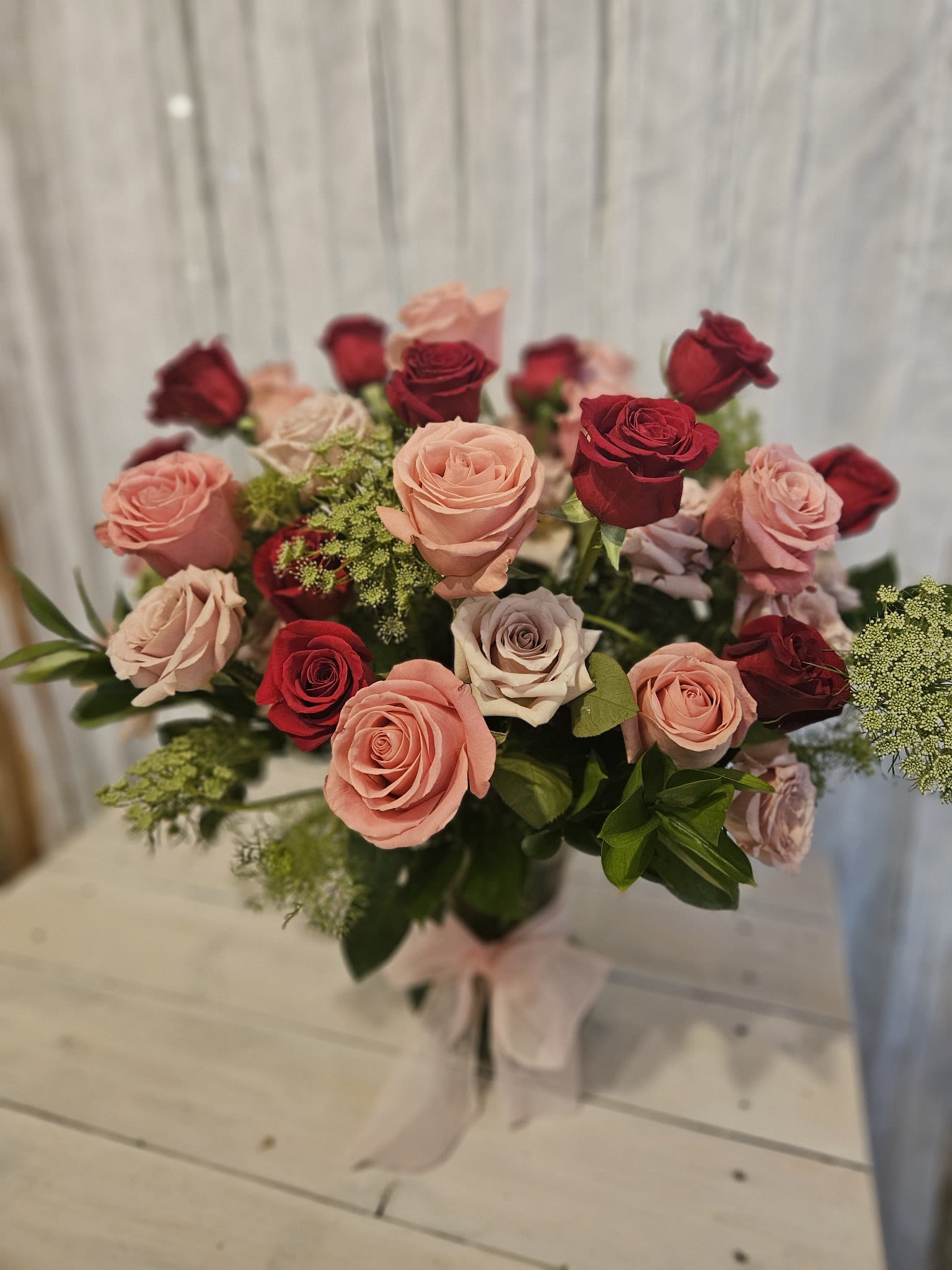 Holy Roses - This romantic show stopper has 3 dozen roses of assorted colors. Masterfully designed in layers to give depth being aesthetically pleasing the eye. Two feet tall, in a beautiful clear fluted Vase.  