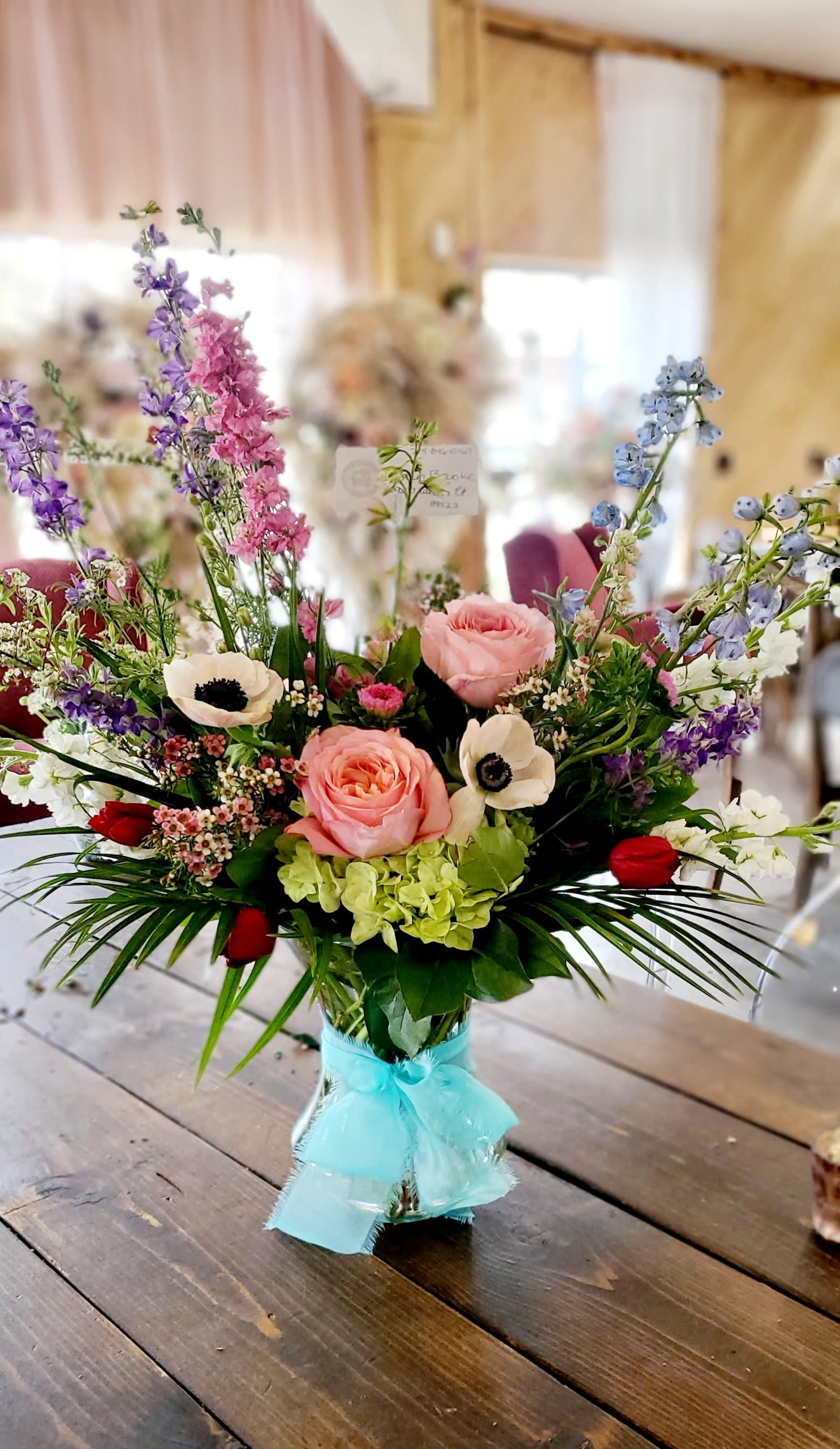 Isn't She Something - This tall standing arrangement is a little bit sassy, a little bit springy. Featuring roses, anemones and palms it makes everything a little more joyful! Send this to somebody who likes things a little more funky and fun.  Approximate Dimensions: 18"D x 18"H