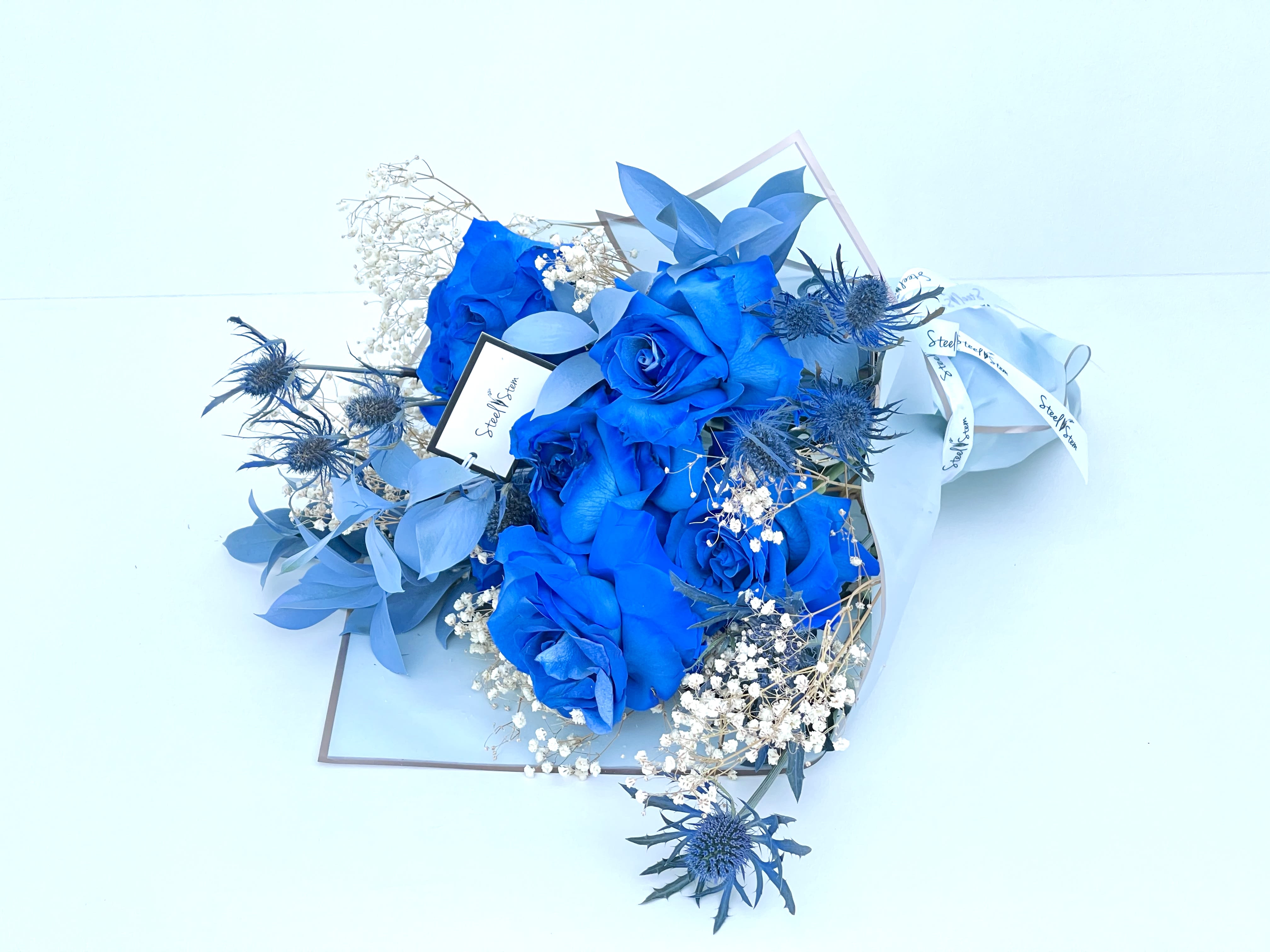 Blue Chic Wrap Bouquet  - This chic wrapped bouquet has a variety of unique  blue roses, baby's breath, blue thistle and Israeli.Wrapped in beautiful wrapping giving the last touch with our Steel Stem ribbon.