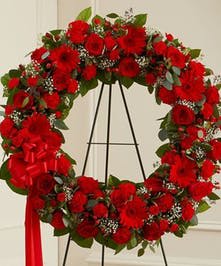 Standing wreath of red flowers with white accents on a black metal easel with red ribbon