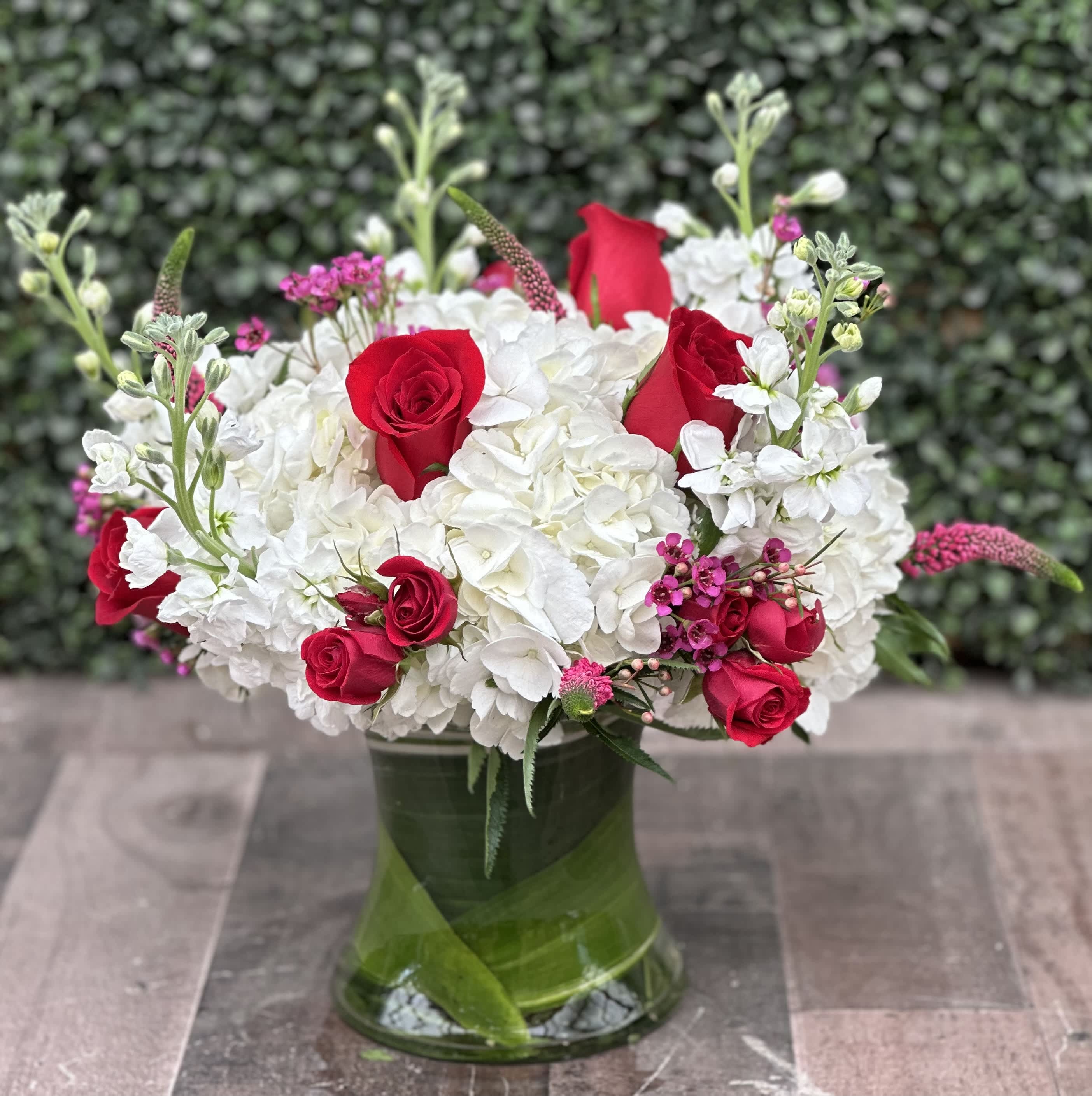 RED PETALS - This clustered arrangement consists of white hydrangeas, red roses, stock, veronica and other flowers and greens.