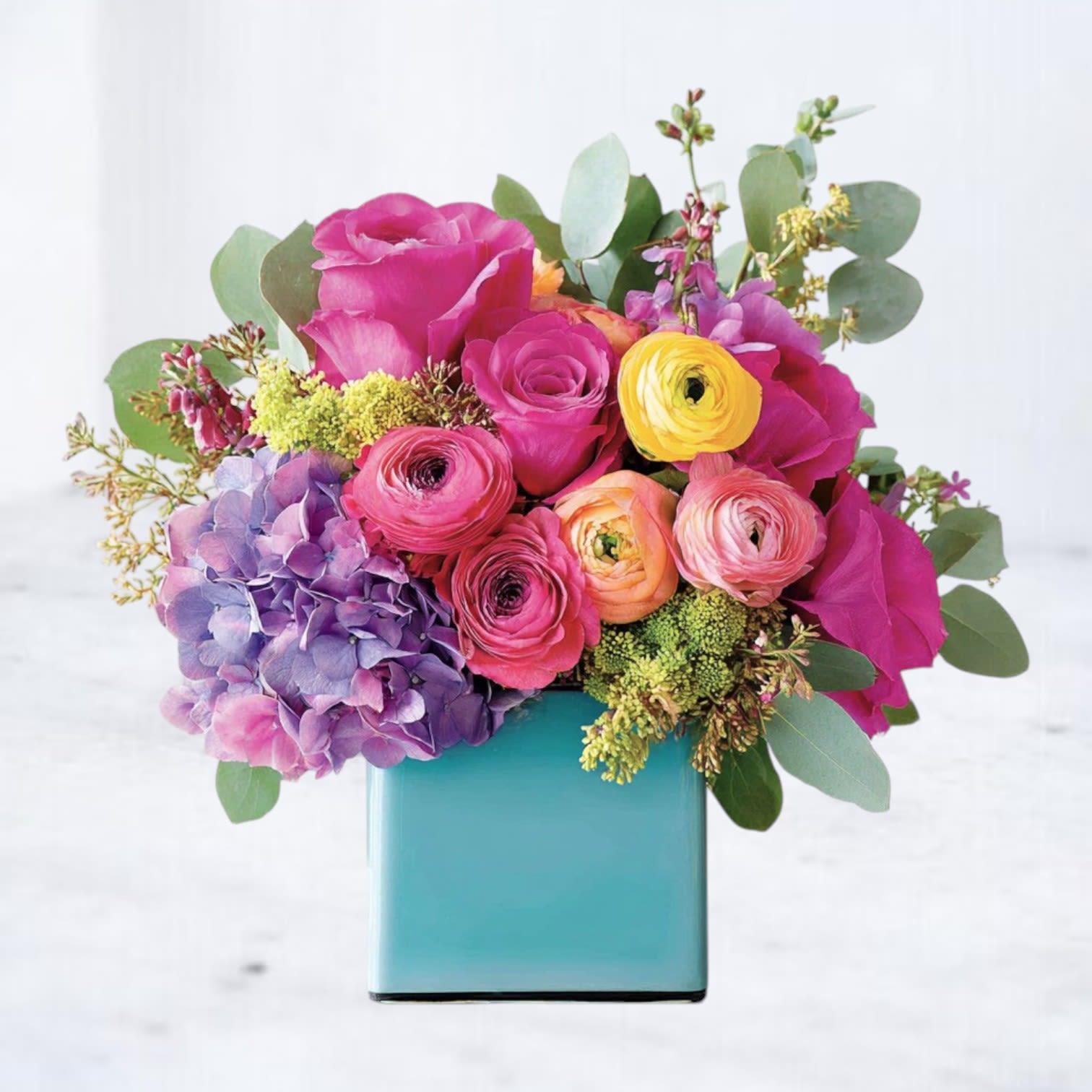 Picturesque - Celebrate their big day in bold, unforgettable color. Our Picturesque arrangement is a vibrant mix of joyful blooms designed to make birthdays feel as bright as they are. Featuring fuchsia anemones, hot pink hydrangea, sunny yellow ranunculus, billy balls, delicate blue tweedia, and sprigs of playful greenery, this design bursts with personality. Handcrafted in a modern teal cylinder vase, this arrangement is ideal for sending birthday cheer across Houston and surrounding areas.  Whether you're celebrating a milestone, a sweet sixteen, or just reminding someone how special they are, Picturesque delivers a punch of happiness with every petal. Available for same-day flower delivery in Houston, Katy, Sugar Land, Cypress, and beyond.