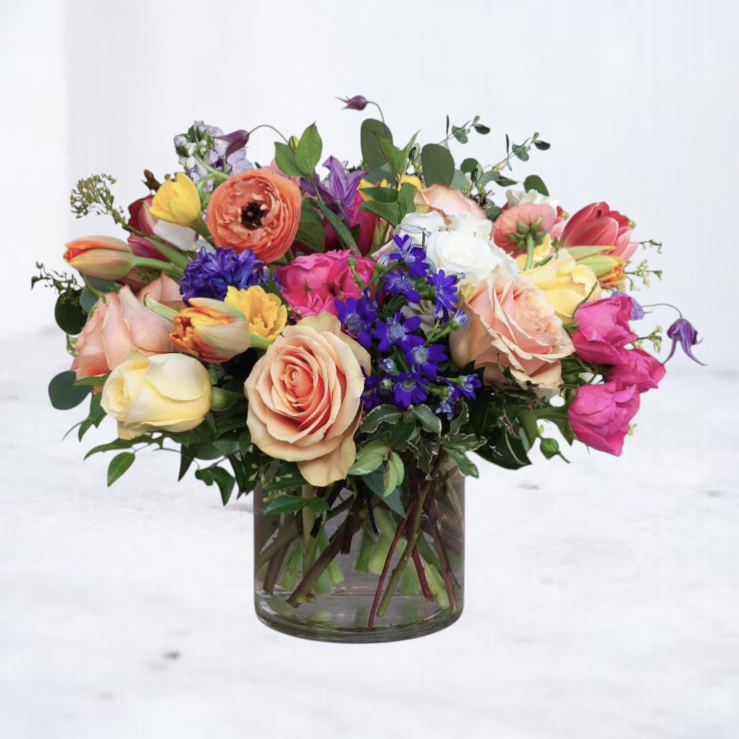 Bravura - A vibrant composition of layered color and texture, this garden-inspired arrangement brings together premium roses, seasonal blooms, and delicate accent flowers in a lush, low design. Soft peach, blush, golden yellow, and vivid violet tones blend effortlessly, creating depth and movement from every angle.  Designed in a modern glass vase, this arrangement feels fresh, artistic, and full of life—perfect for birthdays, celebrations, thank-you gifts, or simply brightening someone’s space. Each bloom is thoughtfully placed to create a natural, abundant look while maintaining a refined, elevated feel.  Available for same-day flower delivery in Houston, Magnolia, The Woodlands, Montgomery and surrounding areas. Flower varieties may vary slightly based on seasonal availability while preserving the overall color palette and style.