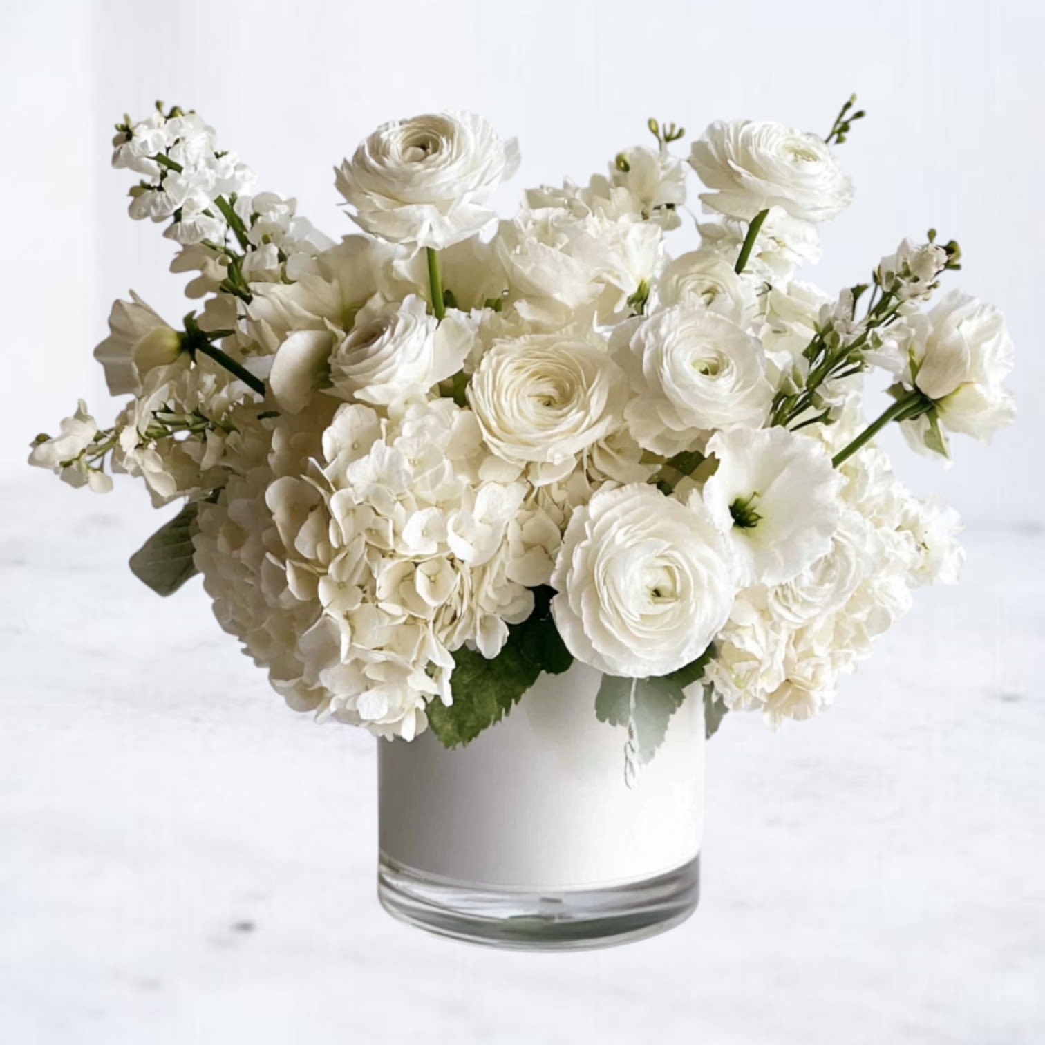Monochrome Garden - Monochrome Garden is a layered all-white composition featuring ranunculus, hydrangea, lisianthus, and fragrant stock arranged in a modern white vessel. Subtle variations in bloom shape and texture create depth while the monochromatic palette keeps the design fresh and architectural.  Refined without feeling formal, this arrangement is ideal for moments that call for quiet elegance — whether you’re offering support, marking a new chapter, or sending something beautifully understated.  Available for same-day flower delivery in Houston and surrounding areas.