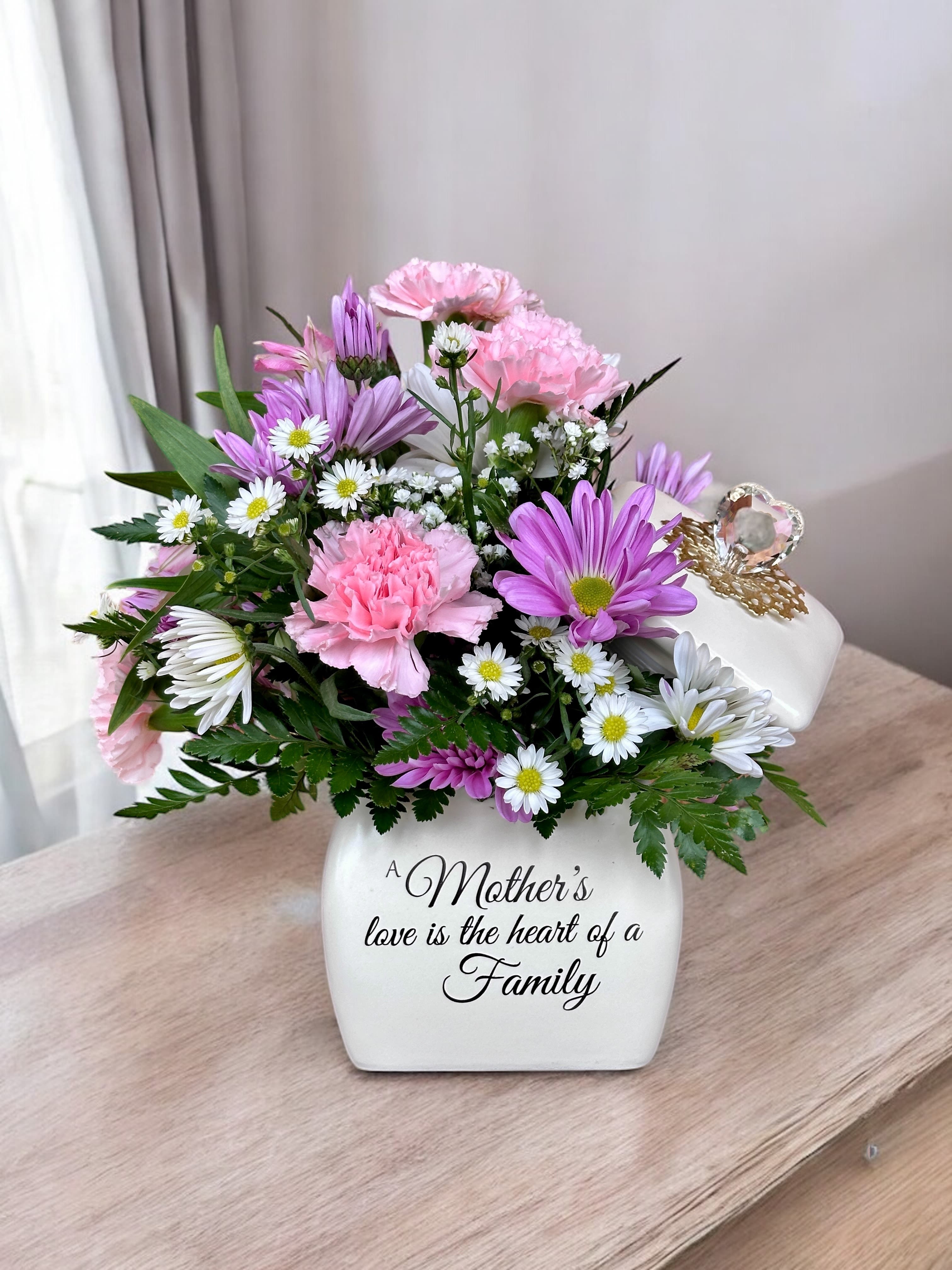 A Mother's Love (SPECIAL) - A mother’s love is the heart of every family. This sentiment is perfectly captured in our garden-inspired bouquet, featuring a mix of pastel blooms in our vintage-inspired canister. Crafted with an elegant glass heart accented by a gold filigree collar, this timeless keepsake is a lasting reminder of the special bond you share.  All-around arrangement with light pink roses and mini carnations, pink limonium and lavender button poms; accented with assorted greenery Artistically designed in our exclusive gift canister, crafted with an elegant glass heart and accented by a gold filigree collar on a ceramic base; features the heartfelt message: “A Mother’s love is the Heart of a Family;” can later be used to hold jewelry/trinkets; measures 4.5"H