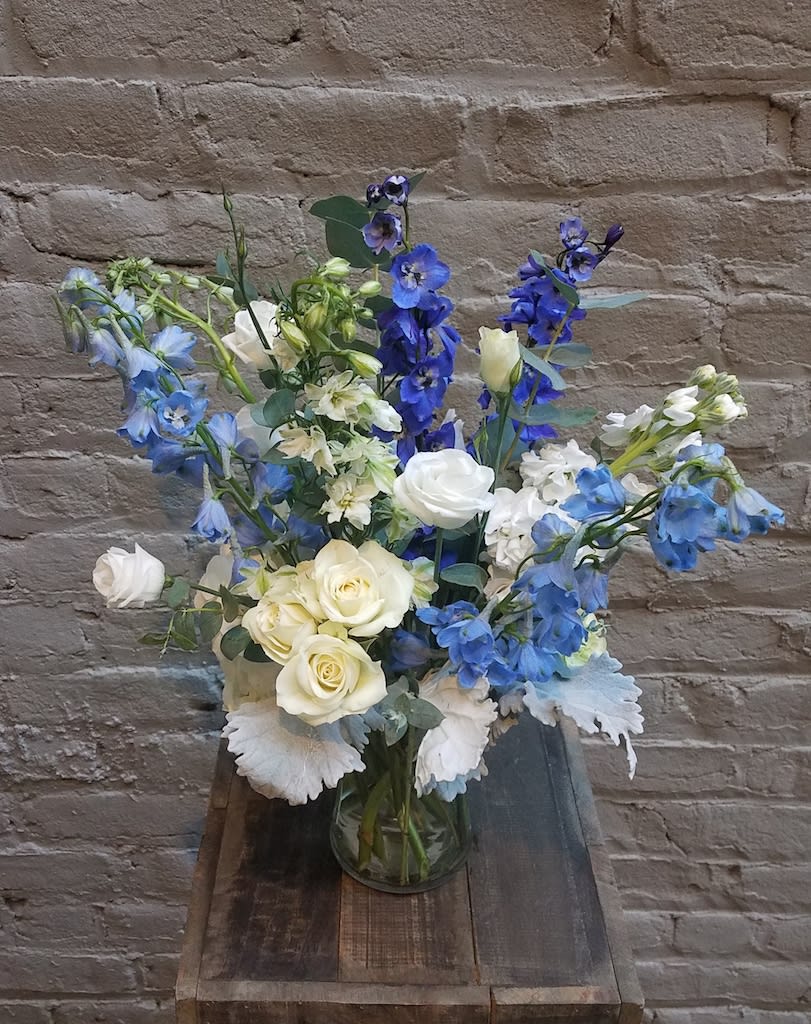 Thinking of Blue - A sweet design in various shades of blues, whites and greens, featuring delphinium, thistle and roses.  Standard arrangement is in a 6" tall clear glass cylinder vase.