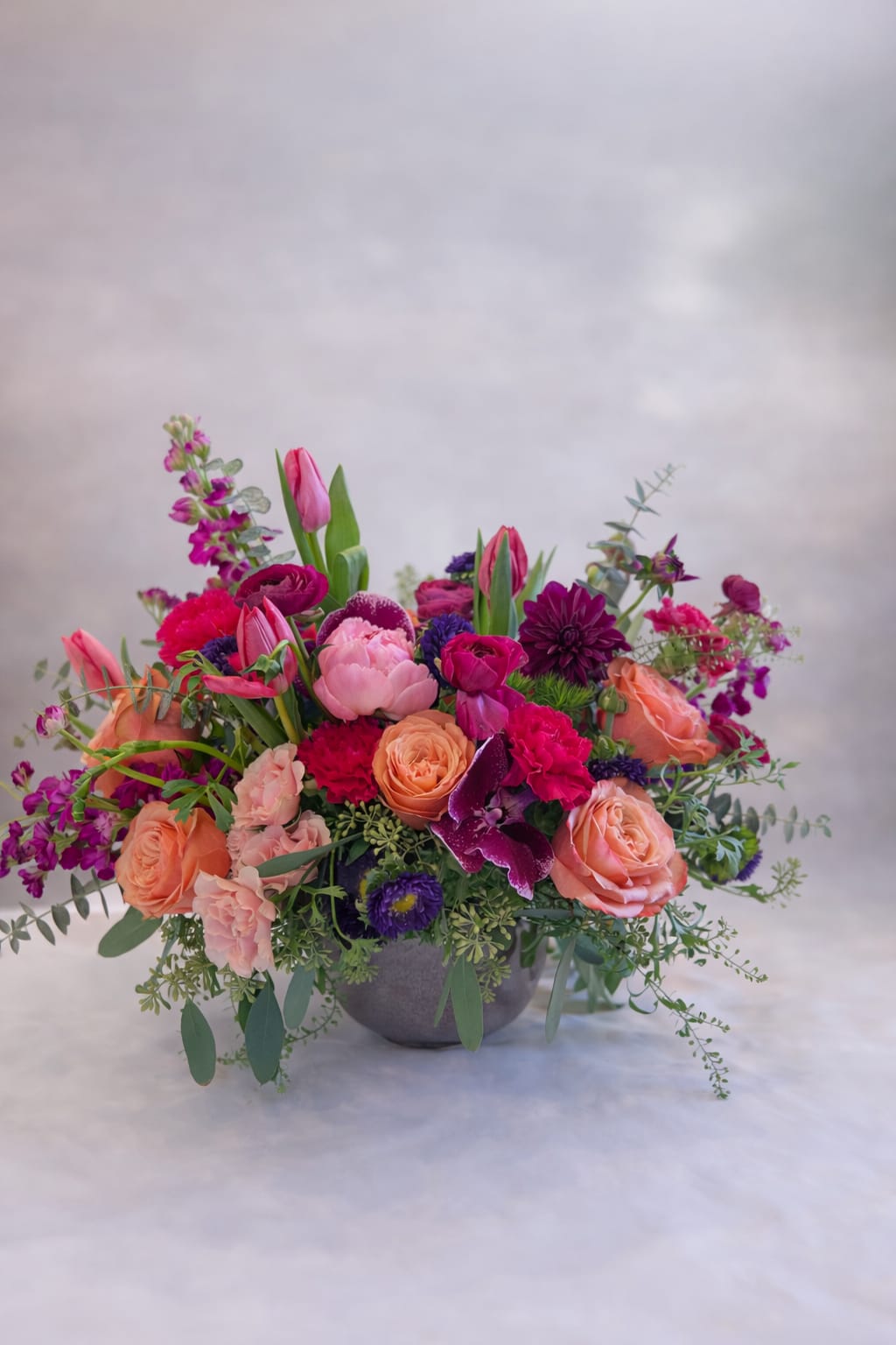 Spring Medley  - Flowers: kahala roses, peonies, dahlias, ranunculus, anemones, tulips, stock, matsumoto, phalaenopsis orchids, spray roses, carnation, dianthus, and eucalyptus. Vase: grey ceramic vase