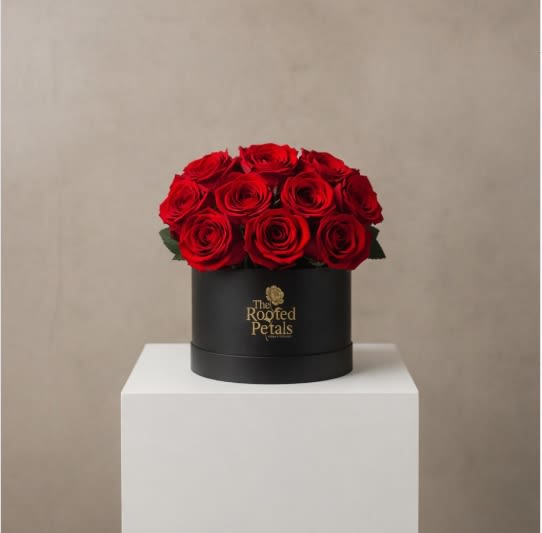 12 Red Roses Hatbox Arrangement - Make a bold and timeless statement with our luxurious 12 Red Roses arrangement. Hand-selected premium red roses are expertly arranged in our signature black hatbox, finished with elegant gold The Rooted Petals branding. Each rose symbolizes deep love and devotion, creating a full, lush dome that speaks romance and sophistication.  Perfect for anniversaries, Valentine’s Day, proposals, or any moment that deserves an unforgettable gesture. This arrangement is designed to impress from every angle and leave a lasting impression long after it’s received. 