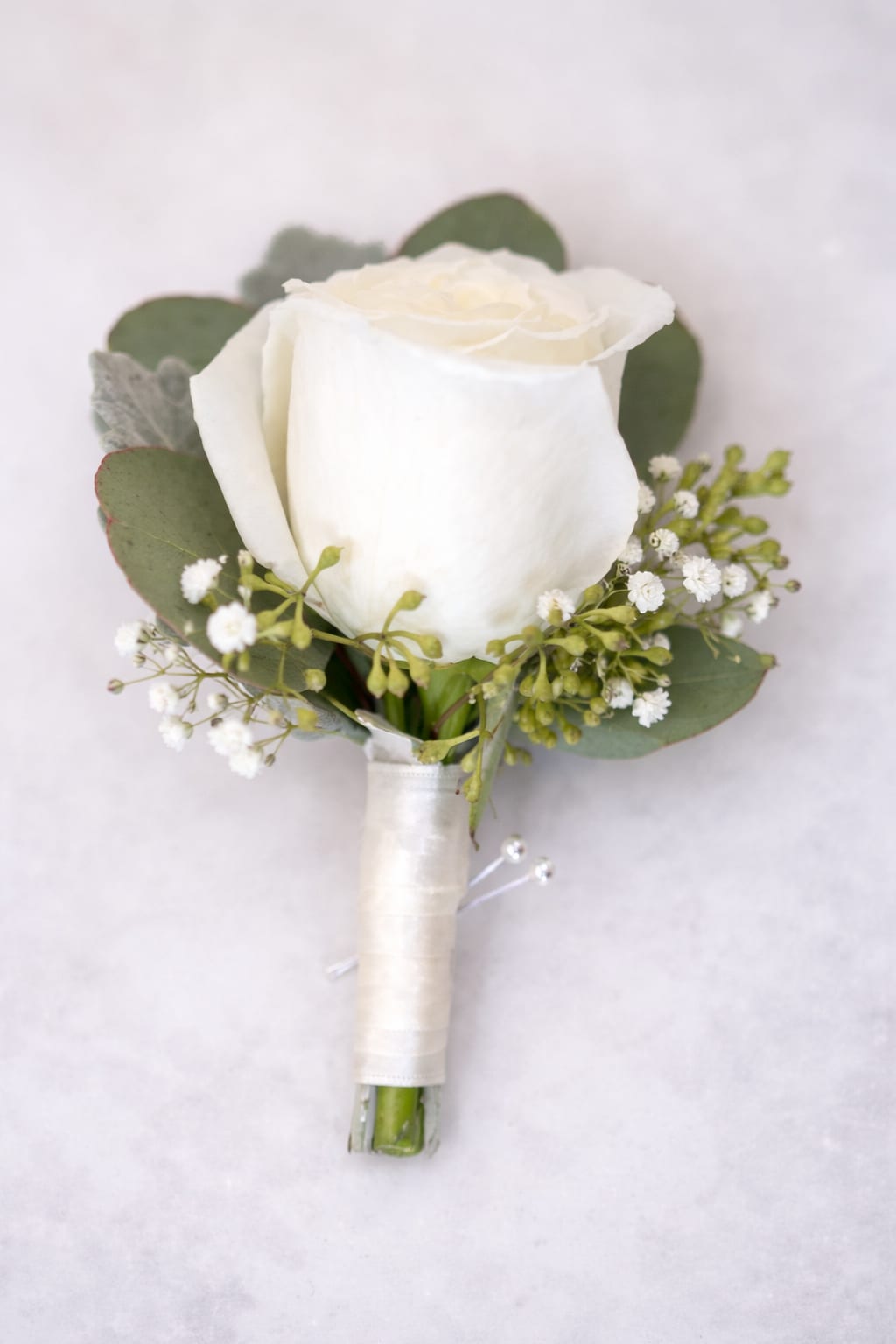 White Rose Boutonnière - A  finishing touch for a wedding or prom. Consisting of a carefully selected red rose complemented with baby’s-breath and greenery, It comes with ribbon of your choice of colors: black, gold, light blue, light pink, purple, silver, or white if the color you desire is not listed please give us a call or write in in "delivery notes" at checkout anyways. If we do not have it we will contact you.   If no ribbon color is mentioned in "delivery notes" at checkout we will make the ribbon White like shown in photo. 