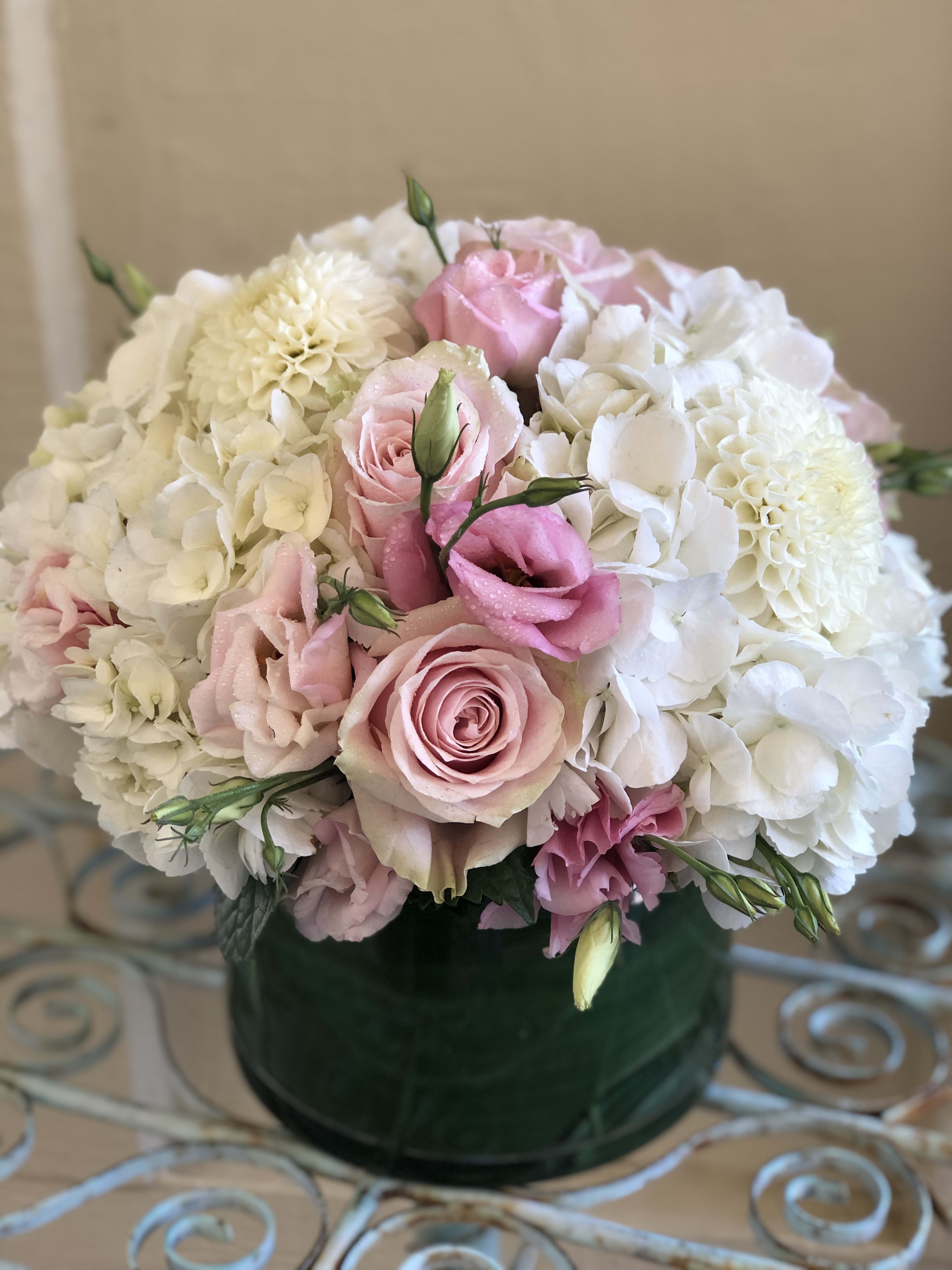 Low round arrangement of white hydrangeas, white dahlias, and pink roses in a green glass vase