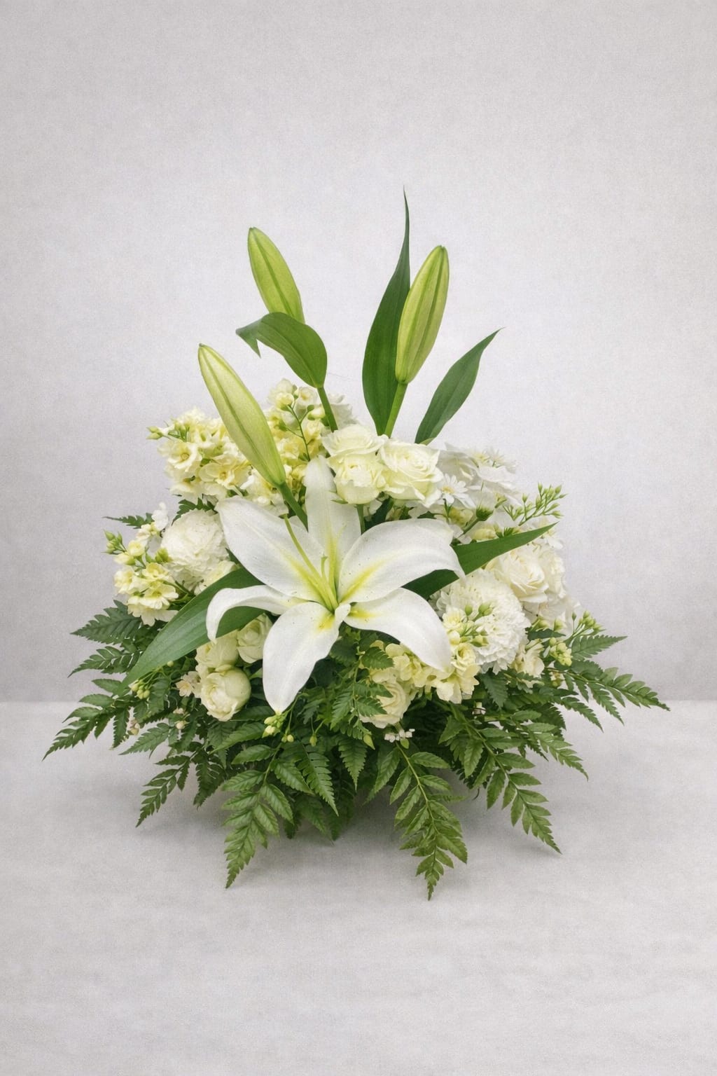 Remembrance - Graceful and calming, Serenity Blooms features white lilies, roses, and seasonal blooms accented with lush greenery. This all-white arrangement is designed to bring comfort, elegance, and quiet beauty to any space or sentiment.  Each piece is Designer’s Choice, created with fresh seasonal blooms. Flowers and colors may vary based on availability while maintaining the overall style and quality.  Better for: Sympathy, Get Well Soon, Mother’s Day, Thank You, New Baby, Thinking of You. 