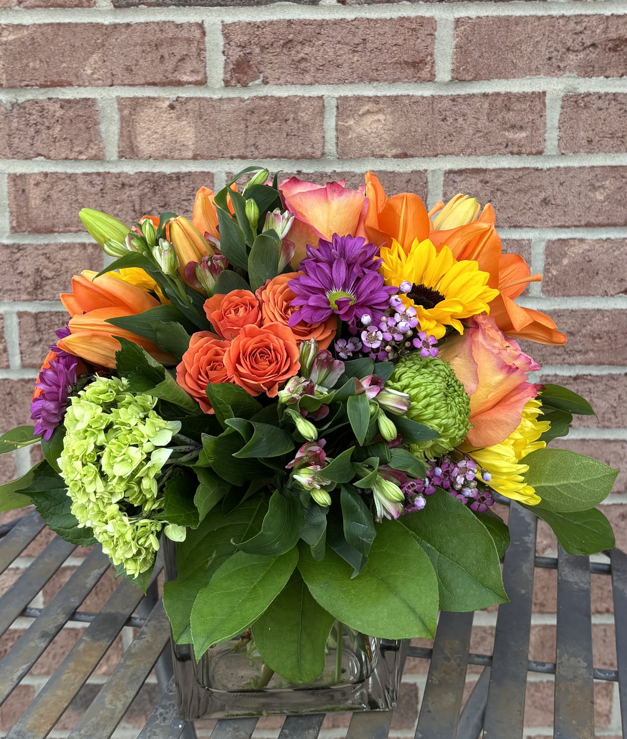 SWEET SURPRISE:  A seasonal square vase arrangement - This modern collection of Designer chosen seasonal blooms spills over a large CLEAR or Seasonal colored square glass vase.  Arrangement is suitable as a Tabletop gift, a hostess or thank you gift, a table centerpiece, a desktop arrangement or for any holiday gifting.