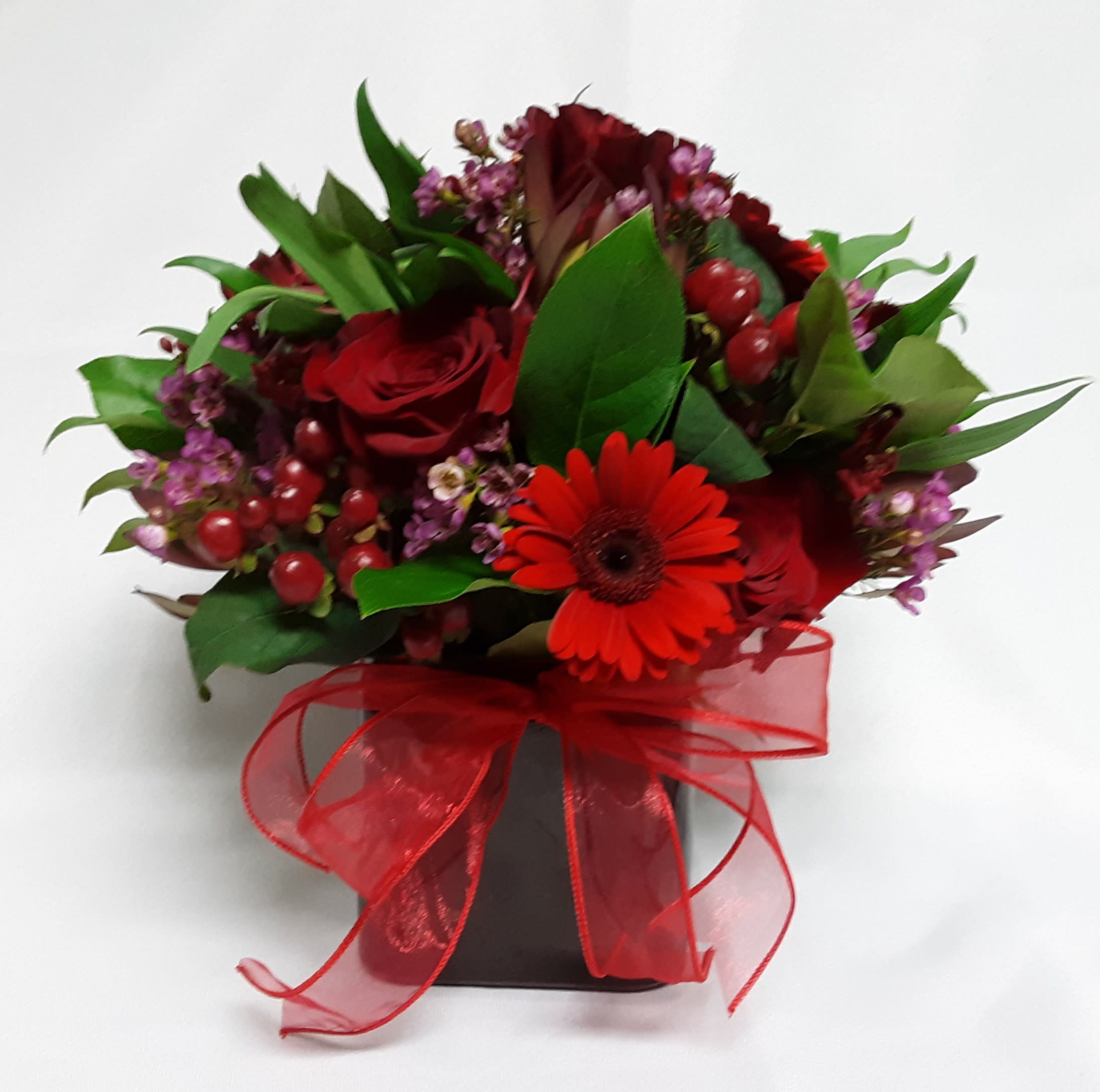 Red Hot - Striking squared style red vase artfully overflowing with designer selected seasonal red blooms &amp; berries, premium greenery, and coordinating filler flowers accents. 