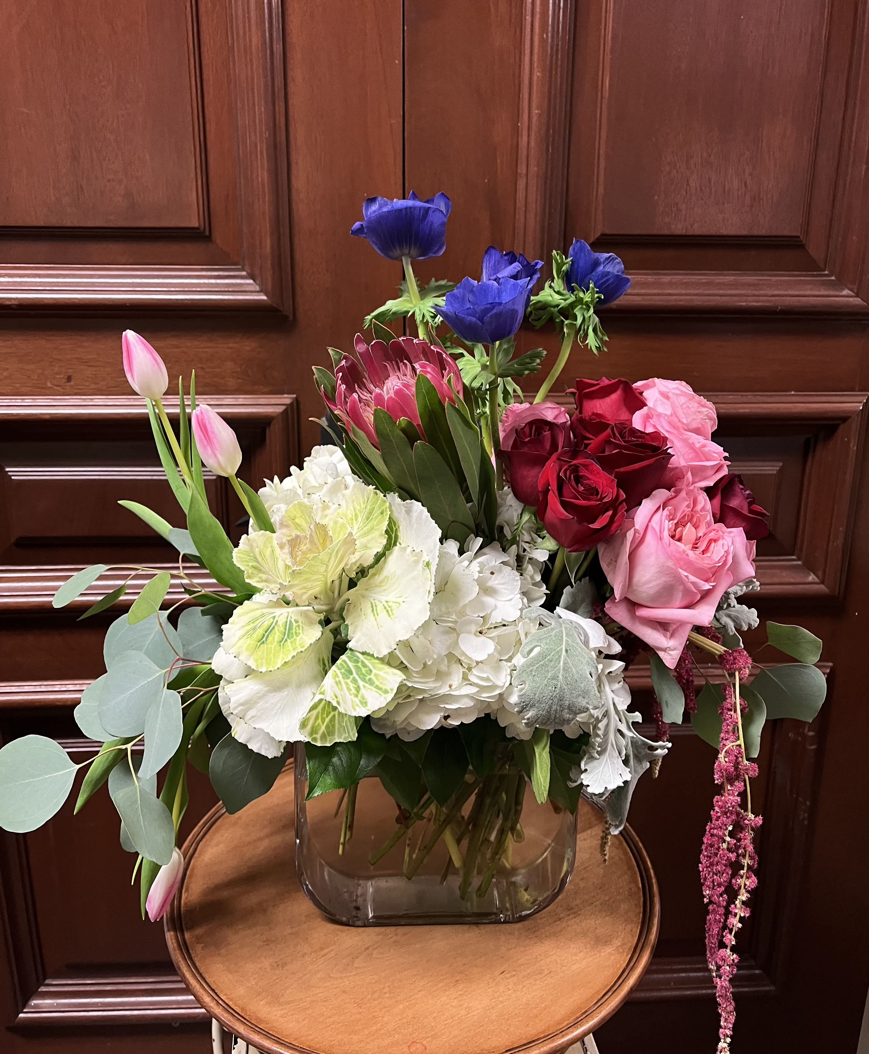 Grand Amour - Recipe: Seasonal Anenomes, Red Roses, Pink English Roses, Pink Tulips, White Hydrangaes, Amaranthus, and Eucalyptus in tall, clear vase. Season: Seasonal Anenomes Design View: Symmetric Front Facing View Photo shown: Standard 