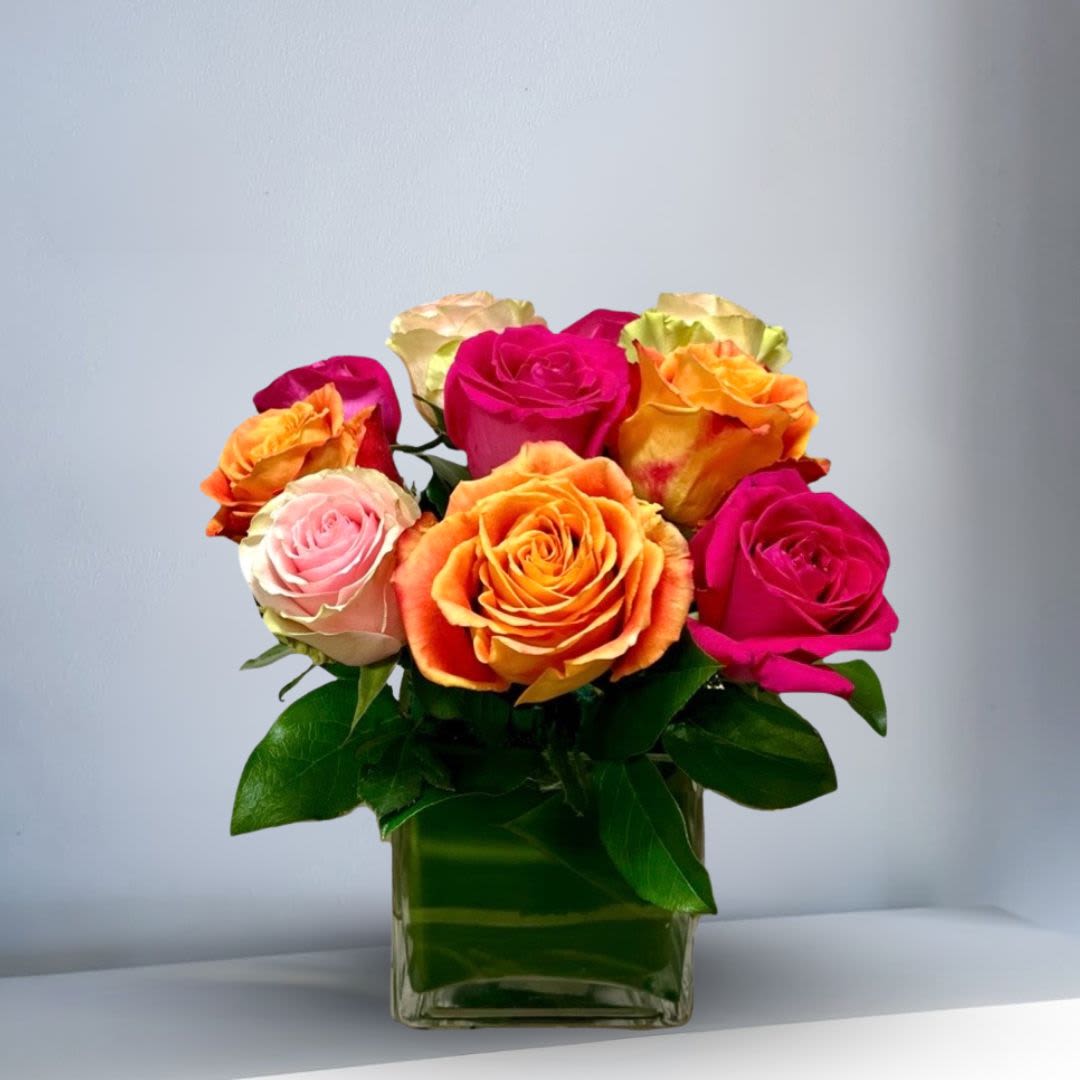 The Modern Roses - Type of Flowers: Dozen short stemmed mix of vibrant roses in a clear, square crystal vase with a leaf wrapped inside. Availability: All Year Round Substitute: Yes Photo Shown: Standard
