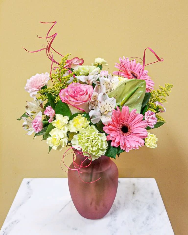 Pink Lemonade - This arrangement of pinks, yellows and greens is as fresh as a glass of pink lemonade.  Designed in a pink glass . approx.  dimensions 15 X 13