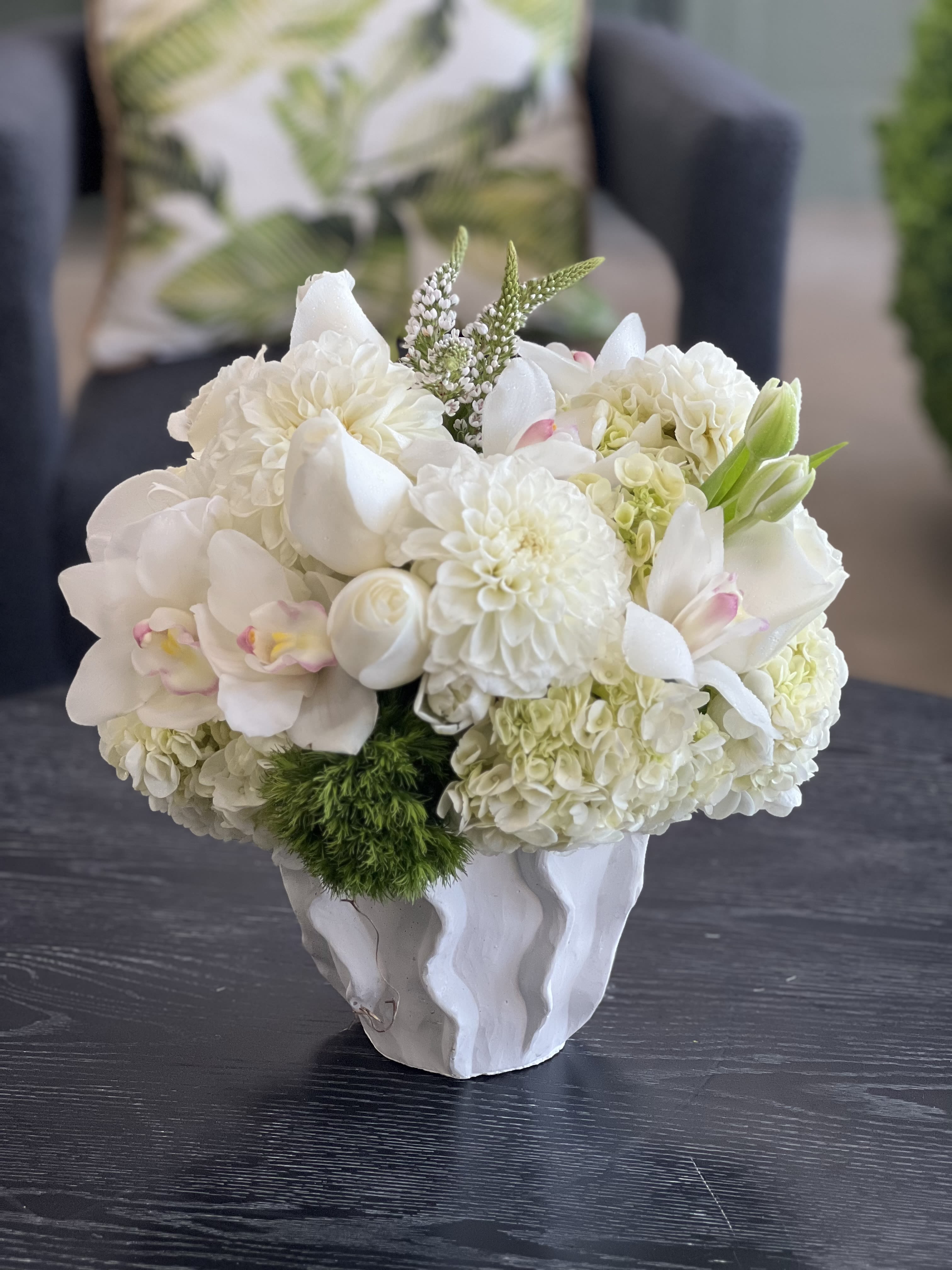 Brittany - This sweet, compact arrangement comprises soft and luscious Hydrangea, with white Dahlias, Roses, Tulips, Veronica, and Cymbidium Orchids in a ceramic vase