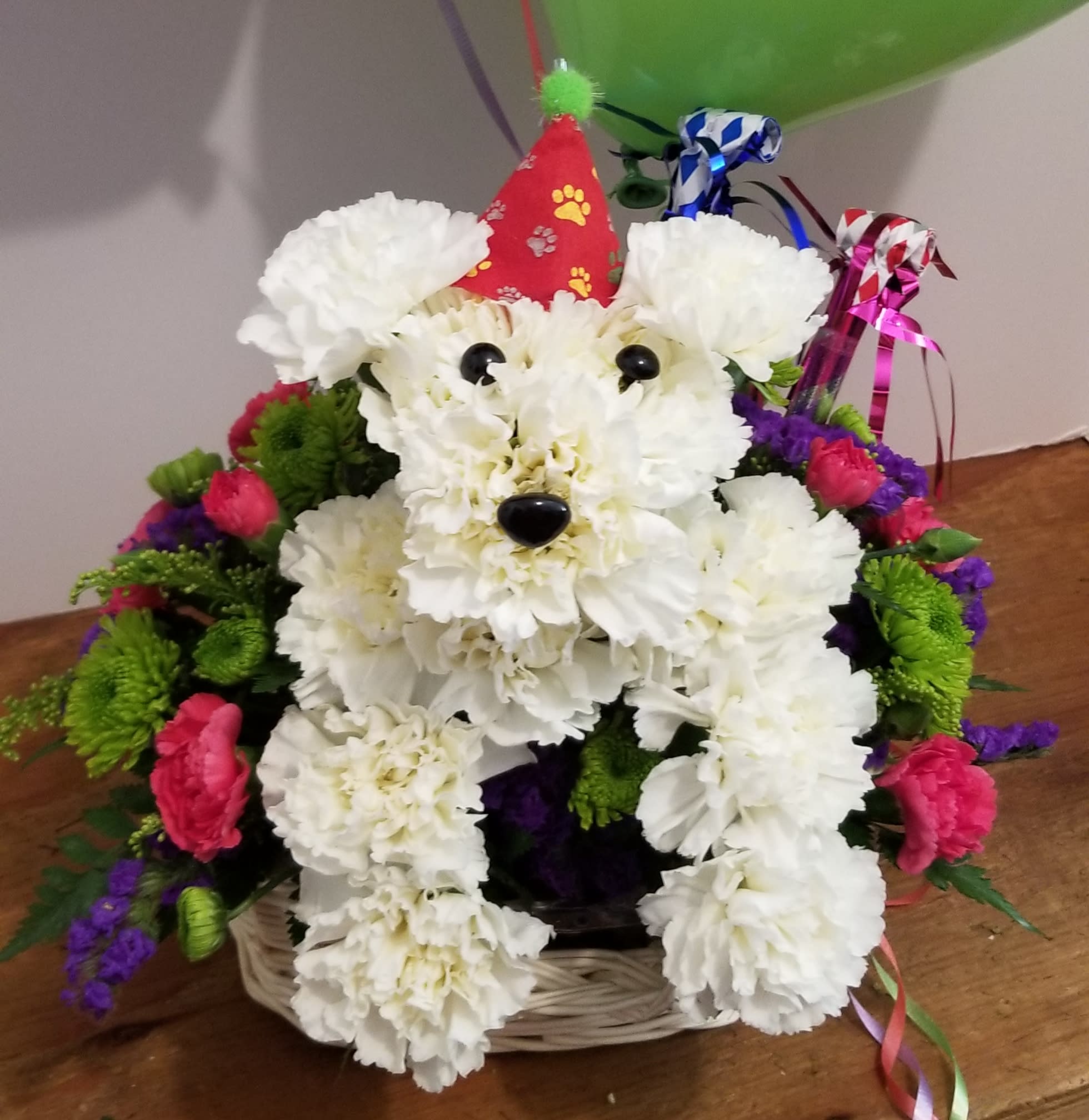 Top Dog Birthday - Put this playful pooch on the invite list for their next birthday bash! Our  Birthday pooch arrangement arrives ready to party 'til the dogs come home, with his adorable birthday hat       (hat may differ than shown). He brings a fun expression of your best wishes for any birthday star (even if they count their age in dog years). Colorful  arrangement of white carnations, poms, mini carnations, statice, solidago and greens  Arranged by FlowerBee's floral artist in the shape of an adorable dog, complete with eyes and nose and party hat and party horns.   Colors, variety and basket may vary to to availability.  Regular price does not include the balloons.  Deluxe price includes balloons.