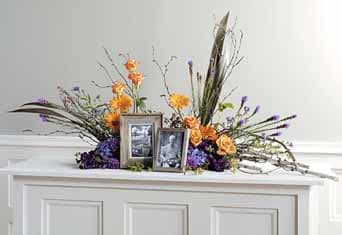 Peaceful Reflections - A timeless tribute designed to honor and remember. Peaceful Reflections features a graceful floral arrangement accompanied by two elegant picture frames, allowing you to display cherished memories alongside beautiful blooms.  Soft orange and green florals create a serene atmosphere, making this the perfect arrangement for memorial services, celebrations of life, or thoughtful remembrance gatherings. PICTURES NOT INCLUDED