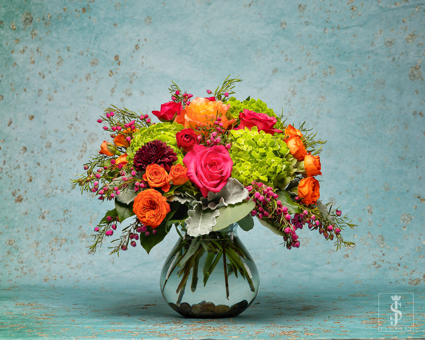 Spring Is Here   - Bold, vibrant and rich colors. Send this bold in colors Designers Choice Mix beautiful arrangement. This arrangement has Orange pink rose, Green Hydrangeas,  Dusty Miller and a mix of spring blooms. 