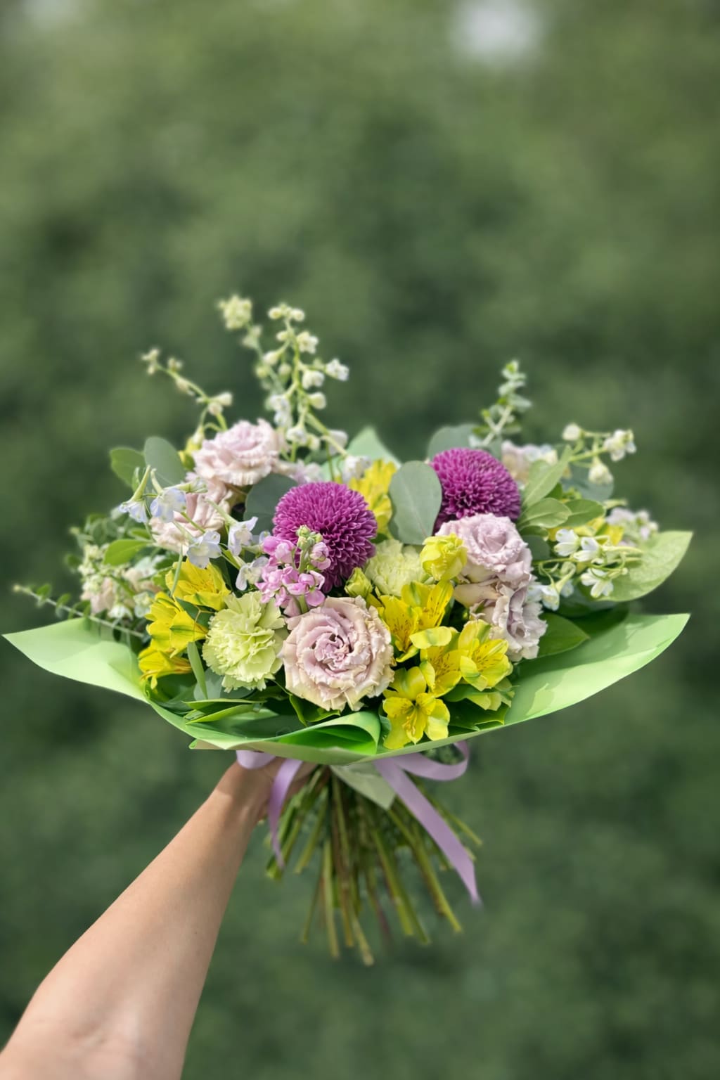 Lavendar Lisi - A sweet juicy bouquet of lavender lisianthus, yellow alstroemeria, light blue delphinium, and adorable green carnations, wrapped in decorative paper and tied in a bow. This is the perfect gift for your niece's dance recital or birthday. 