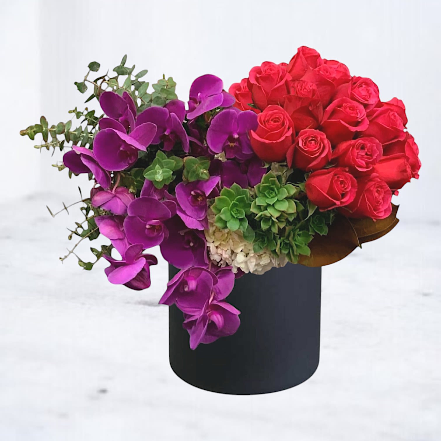 Redolent Heart - Luxury Red Rose and Orchid Flower Arrangement for Romantic Occasions Turn up the passion with Redolent Heart, a bold and breathtaking floral arrangement designed to leave a lasting impression. This luxury flower arrangement features an opulent cascade of deep magenta phalaenopsis orchids, rich red roses, creamy hydrangea, and lush succulents—all artfully arranged in a chic black vase.  Whether you're celebrating an anniversary, planning a romantic date night, or searching for the perfect "I’m sorry" flowers, Redolent Heart delivers both drama and devotion.  