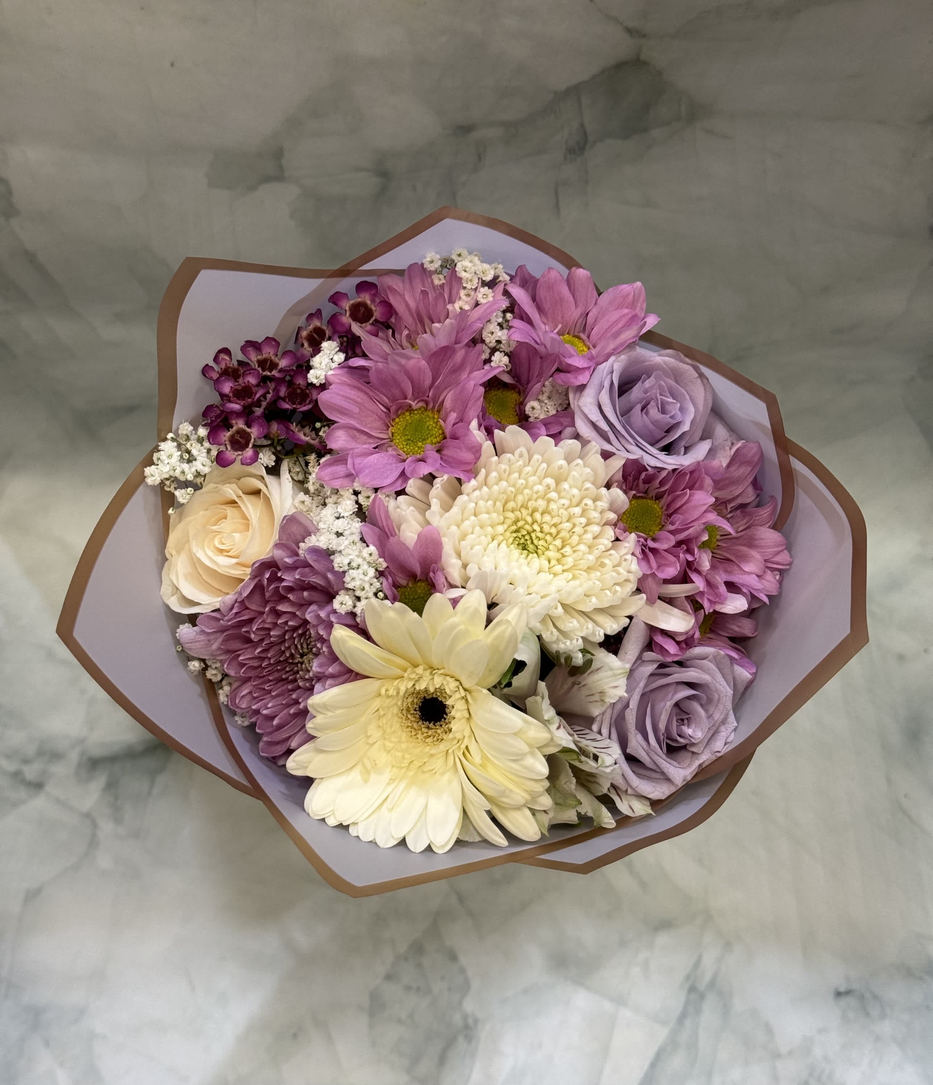 White and Lavender Blooms - This beautiful white and lavender bouquet is wrapped in our special floral wrapping paper and tied with a bow. This is the perfect gift for graduation or any other happy occasion where you want to make that special person in your life feel a bit more special. The flowers included in this bouquet are Pom Pons, Mums, Gerber Daisies, Alstromeria, Roses, Babies Breath, and Wax. 