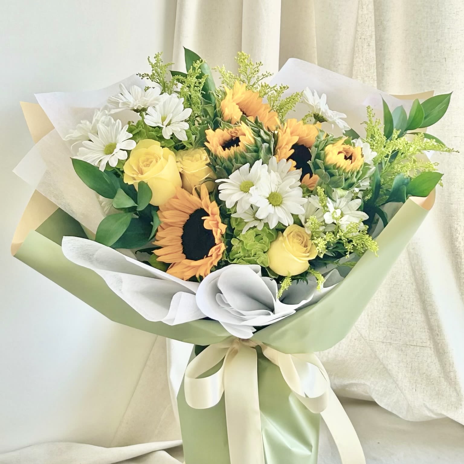 Jolene  - A front-facing bouquet with yellow and green flowers, wrapped in green and peach two-tone paper.   Flower types may vary depending on the season.