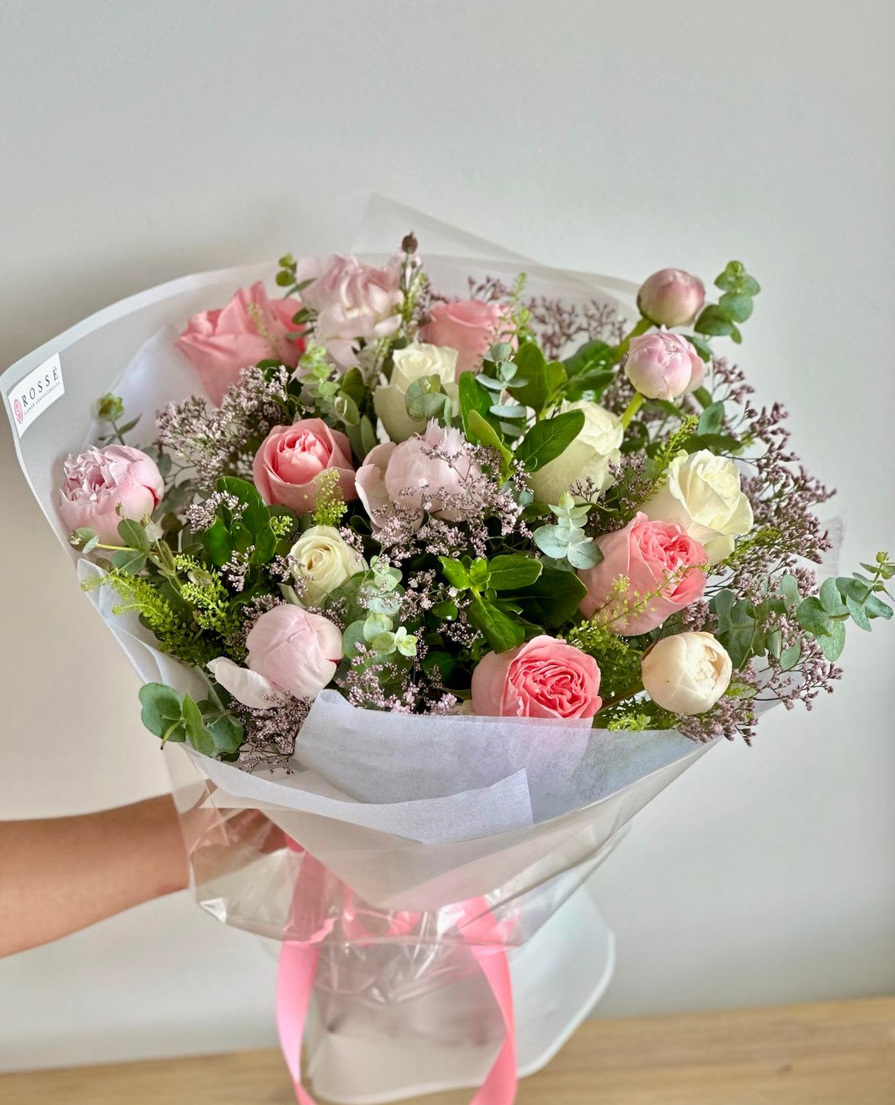 Peony Garden   - A round bouquet of white and pink flowers with lush greenery, wrapped in white paper.   Flower types may vary depending on the season.