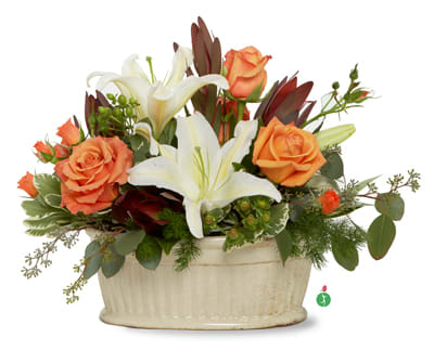 Arrangement of white lilies and orange roses in an oval cream ceramic container