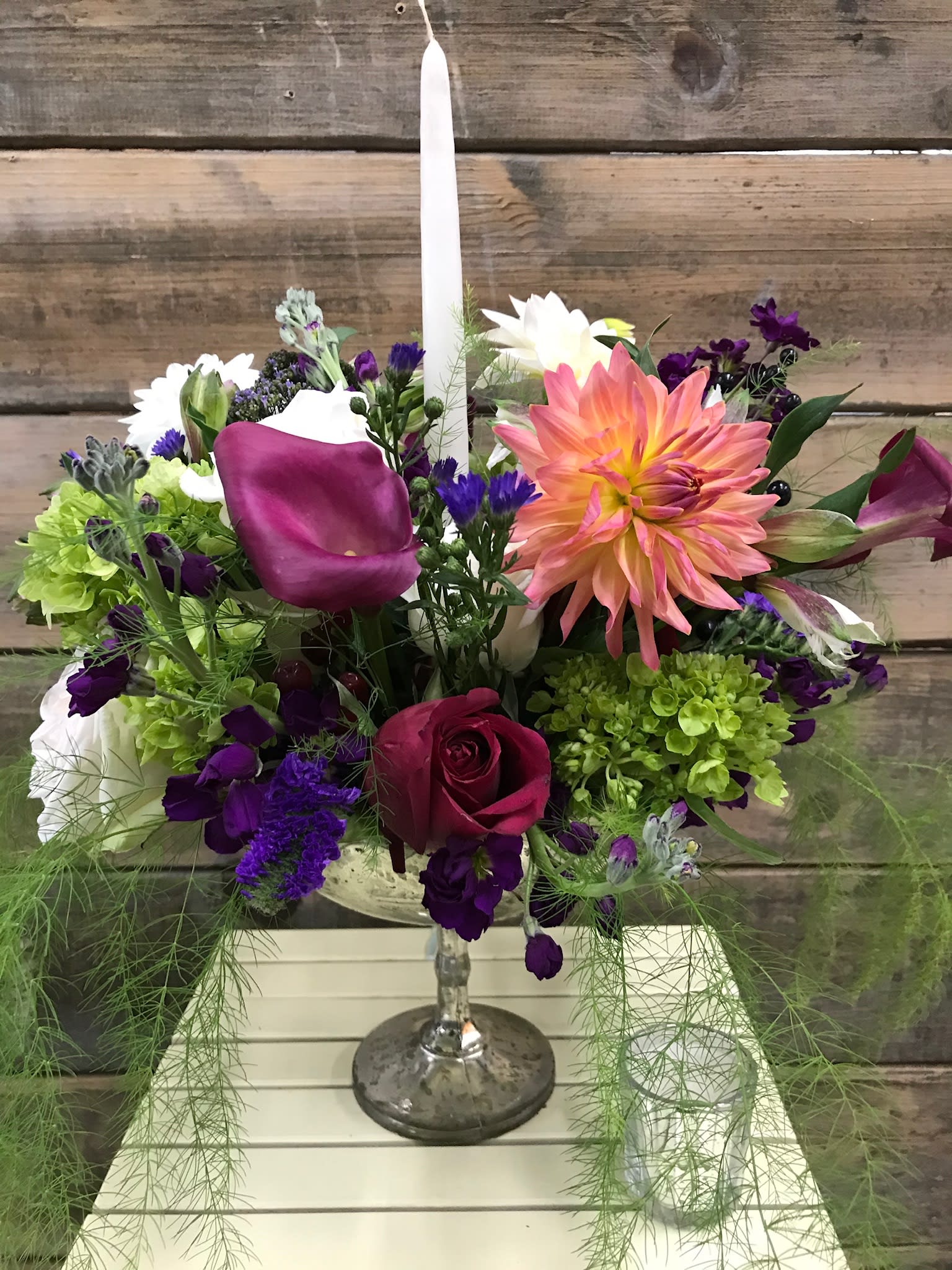 Candlelight Dinner. - With a Covid world we have to make changes in our routine. An intimate romantic, candlelight dinner might lift the mood and could be fun.This centerpiece  is designed with seasonal blooms and greens, you can request the color of your candle and if we don’t have it in stock we will pick something very close to your choice.