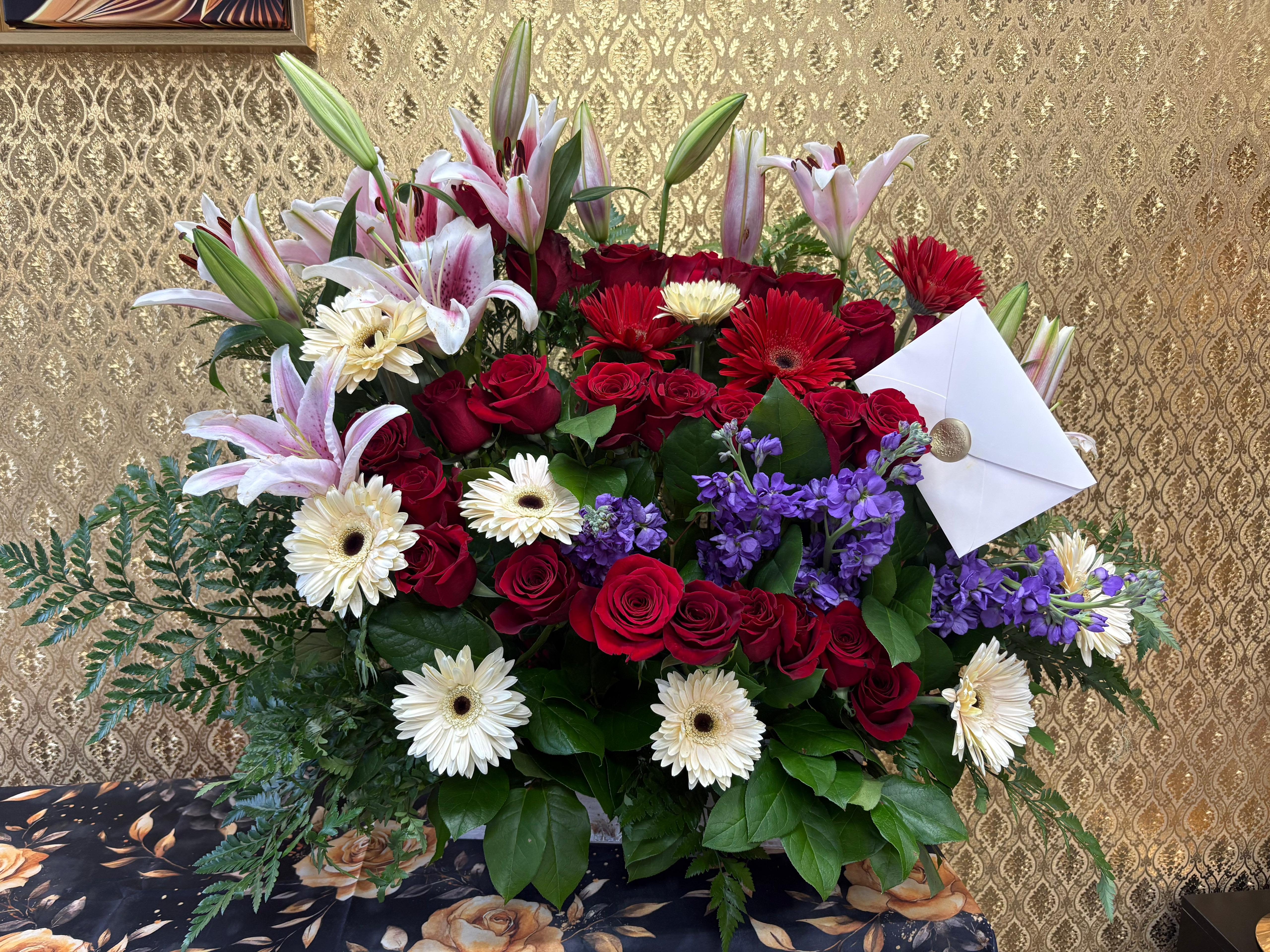 Love at first SIGHT PLATINUM ARRANGEMENT - Red roses symbolise love and romance. The meaning of the red rose comes from ancient spirituality and literature. In classical literature and art, red roses often represent sacrifice, beauty and the transience of life.  At ELLIE FLOWERS AND COFFEE SHOP, our florists have created this luxurious arrangement, featuring 50 premium red roses, red and white gerberas, pink lilies, purple flowers, baby breath and greeneries, in a large base.  Includes a “i love you” card with envelope, please send your card message with the order.