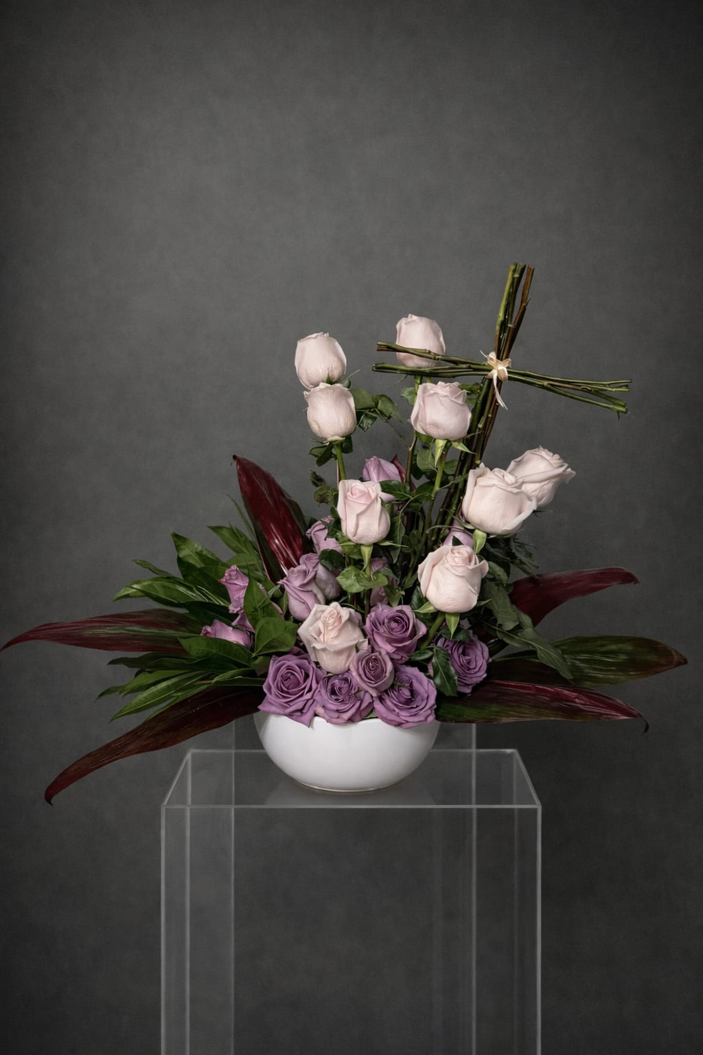 Serenity  - A deeply heartfelt sympathy tribute featuring lush, velvety roses and rich exotic foliage, gracefully accented with a beautifully structured cross. A timeless and elegant expression of love, compassion, and unwavering support — thoughtfully crafted to bring comfort and solace during life's most tender moments.