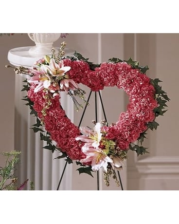 Our Love Eternal - To remember a loved one this pink heart wreath is a lovely expression. Pink carnations are tightly designed and accented with pink lilies waxflower and hydrangea blossoms. Delivered on an easel for display.   FCS19-3560