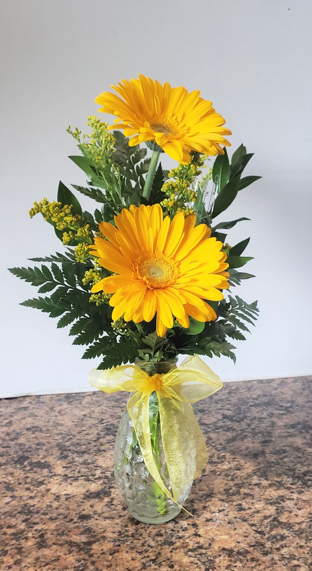 Sunshine Grace - Sunshine Grace features cheerful yellow gerberas paired with fresh greenery in a classic glass vase — a reminder of the warmth and positivity she brings into our world. Perfect for honoring mothers, daughters, sisters, coworkers, and the women who uplift us daily.