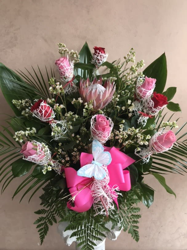 Blushing Protea  - This arrangement features red and pink long stem roses with a king protea in the middle, decoratively arranged in a floral foam container.  Whether it's for a specific occasion or just because, this arrangement makes the perfect centerpiece for any room and is sure to bring joy and happiness to the person receiving it.  Deluxe and Premium sizes will feature more flowers for an even fuller looking arrangement. 