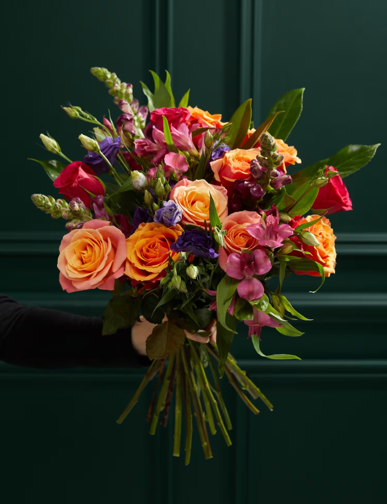Radiant Bloom Symphony - Bring vibrant bursts of color to your home with this stunning 25-stem bouquet. Featuring a cheerful mix of coral and orange roses, blue lisianthus, cerise snapdragons, and cerise alstroemeria, complemented by lush greenbell and laurel foliage, this arrangement radiates summery charm. Its bright and uplifting palette makes it the perfect gift to brighten someone's day or send as a thoughtful gesture to a friend in need of a mood boost. Please note, colors may vary slightly throughout the season for a unique touch.  What's included?  25 stems, including Cerise Alstroemeria, Orange Roses, Blue Lisianthus, Burgundy Snapdragons, Laurel, Peach, and Cerise Roses.