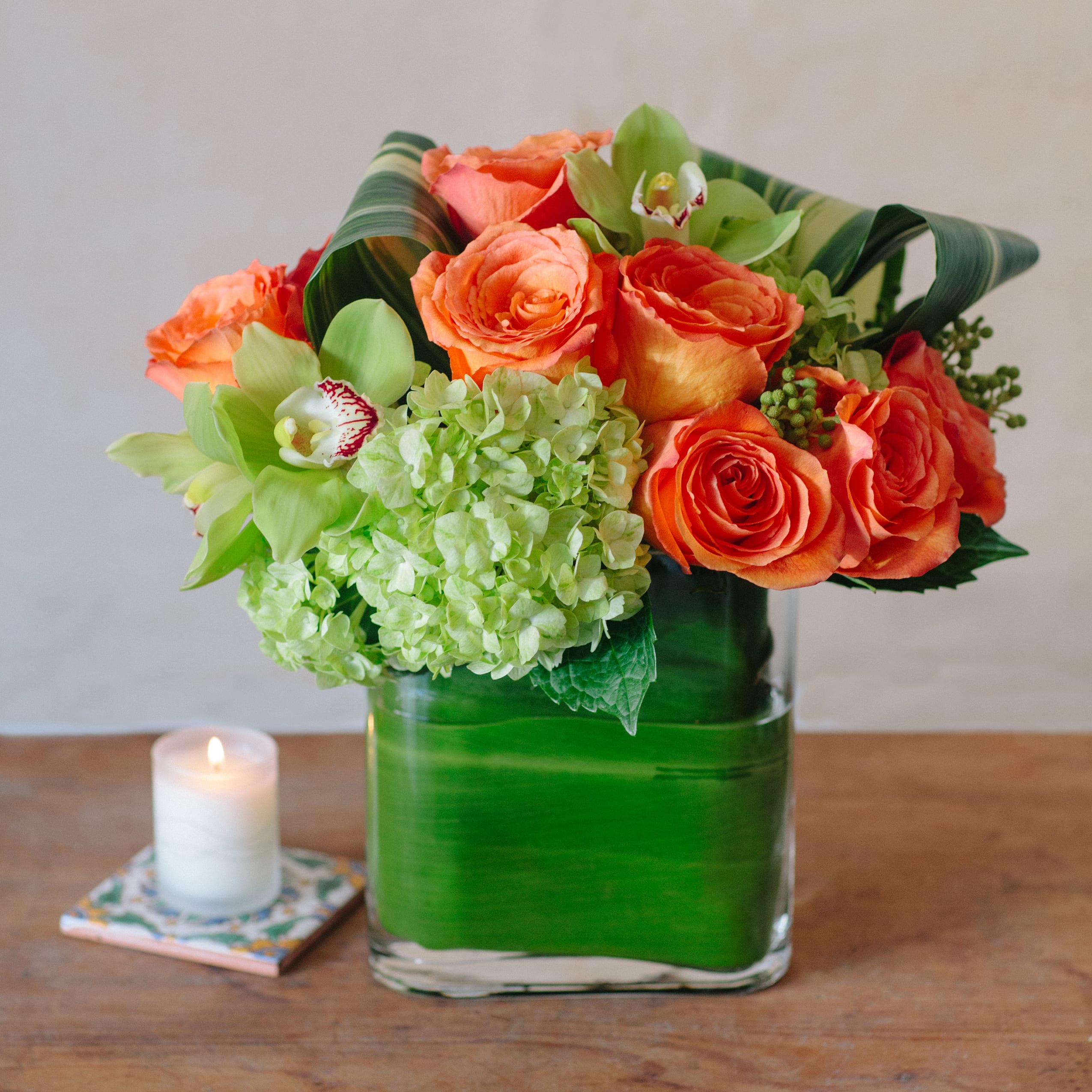 Envelope full of flowers - This is a ti leaf lined envelope shaped vase beautifully filled with cymbidium orchids, roses and hydrangea. This is a modern take on an arrangement that is perfect for the office or on a side table in the home. Lush and modern flowers are a perfect gift!   NOTES: This picture is representation of the color palette. While a lot of the flowers will be sourced, some may need to be exchanged with comparable or higher quality flowers. We will choose the freshest and most interesting ingredients at the market to make this arrangement shine. Vessels may be substituted depending on availability.  