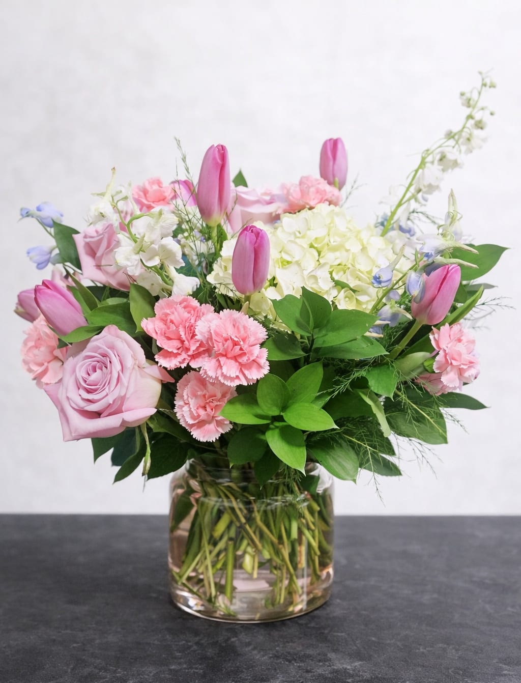 Blush garden elegance  - A soft and romantic garden-style arrangement featuring blush roses, pink tulips, hydrangea, and delicate carnations in a modern glass vase. Perfect for anniversaries, or just because.