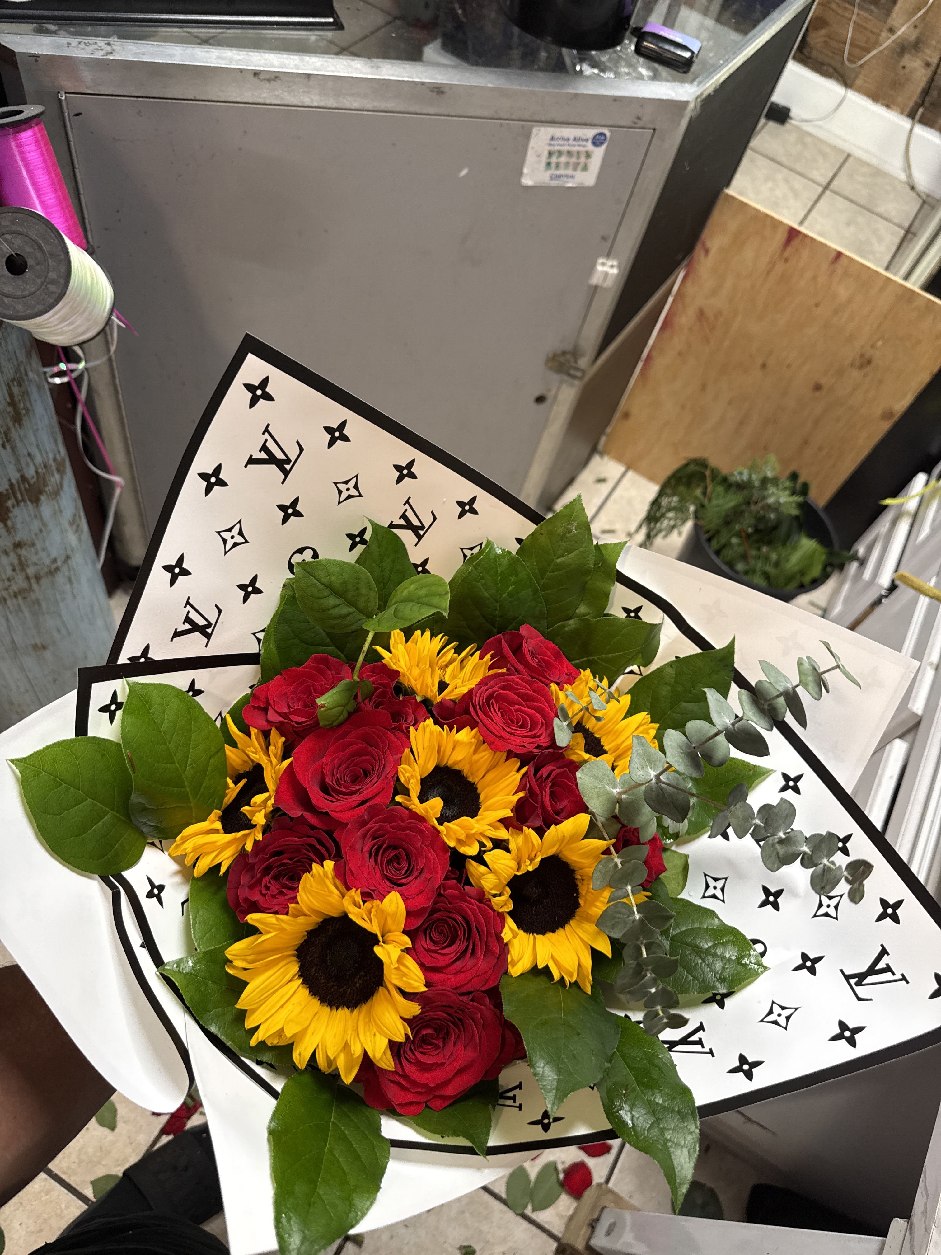 Sunflowers n Roses - ​Floral Mix: Premium red roses, vibrant sunflowers, and fresh eucalyptus accents. ​Packaging: Hand-wrapped in our signature designer-inspired monochromatic paper for a luxury finish. ​Perfect For: Anniversaries, "just because" moments, or brightening up a modern living space.