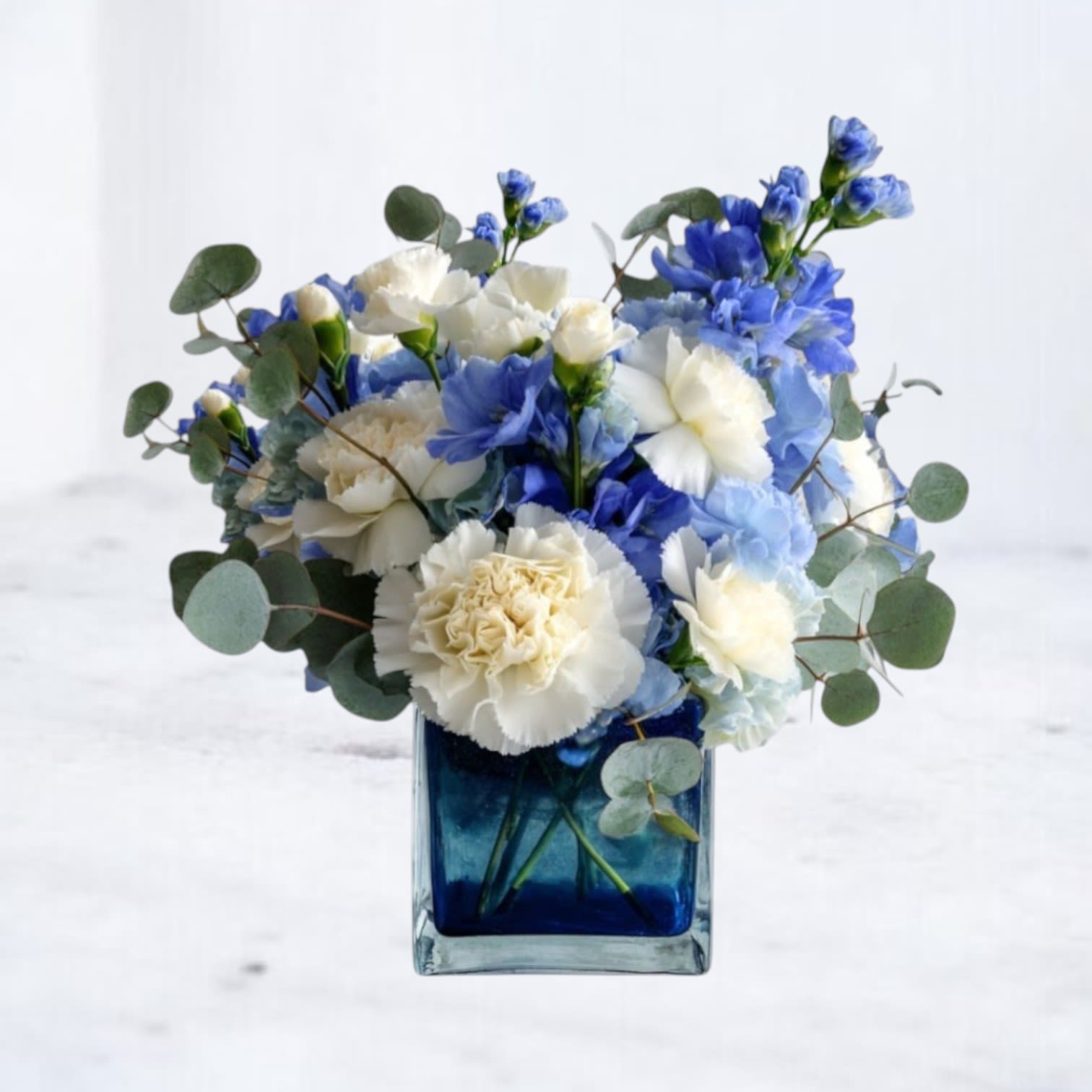 Bundle of Blooms – Baby Boy - Celebrate a sweet new arrival with our Bundle of Blooms – Baby Boy floral arrangement. This soft and cheerful design is arranged in a keepsake baby block vase and features crisp white ranunculus, lisianthus, and roses accented with charming blue delphinium, waxflower, and a playful polka dot ribbon. It’s a thoughtful way to welcome a newborn, congratulate new parents, or decorate a nursery in Galveston, Texas and surrounding southern Houston communities.  Perfect for hospital deliveries in Galveston, home celebrations in Clear Lake, or baby showers in League City, this baby boy flower arrangement is sure to bring smiles and sentiment.  Substitution Policy: At Twigs and Blooms, we use only the freshest flowers available. In the event that any elements are unavailable, we will thoughtfully substitute with similar blooms or a comparable container of equal or greater value—while always maintaining the integrity and color palette of the original design. Every arrangement is made with care to honor your intention.