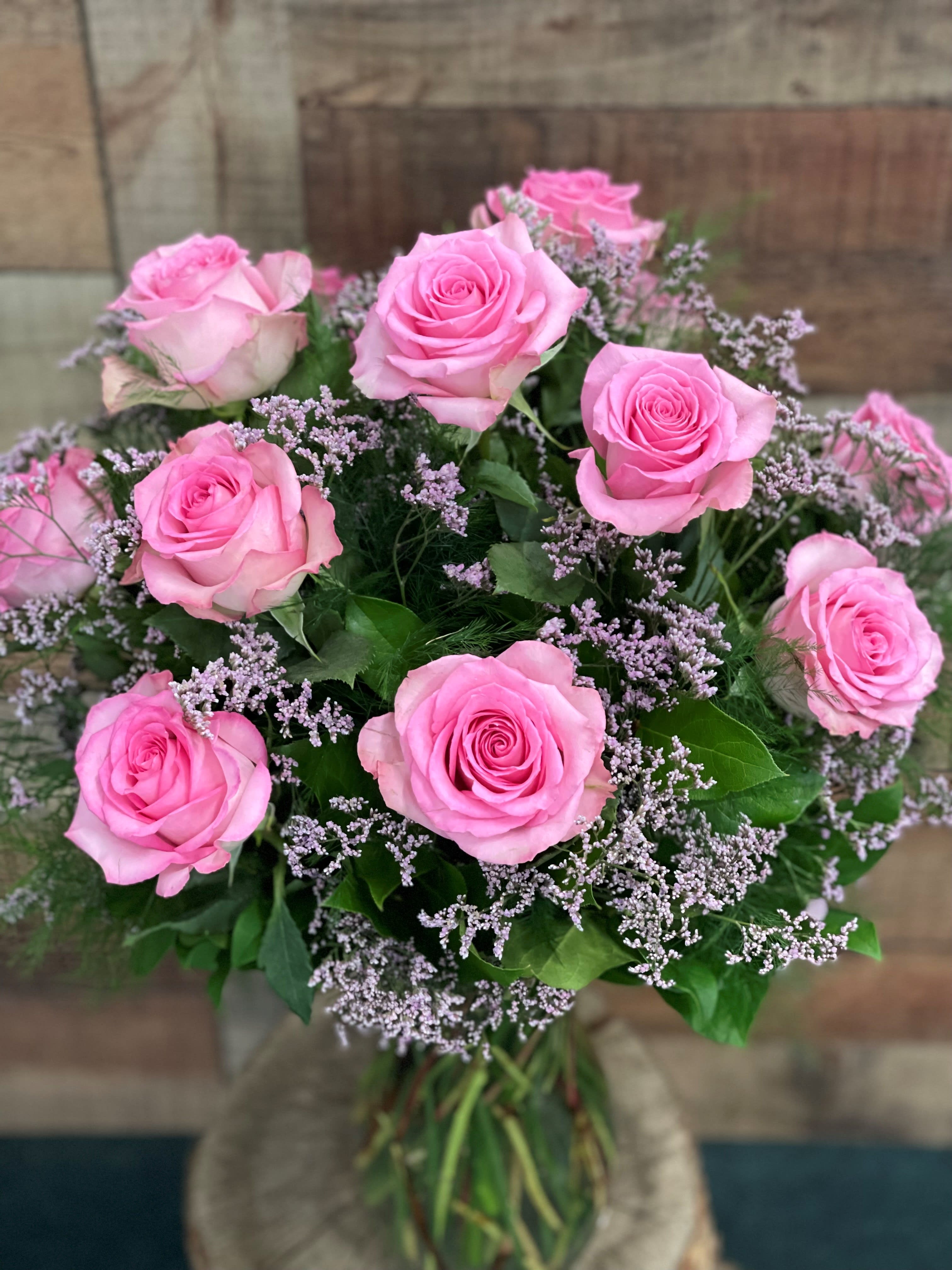 Premium Dozen Pink Roses - 12 Premium long stem pink roses artfully arranged in a recycled clear glass vase with greens and seasonal filler.