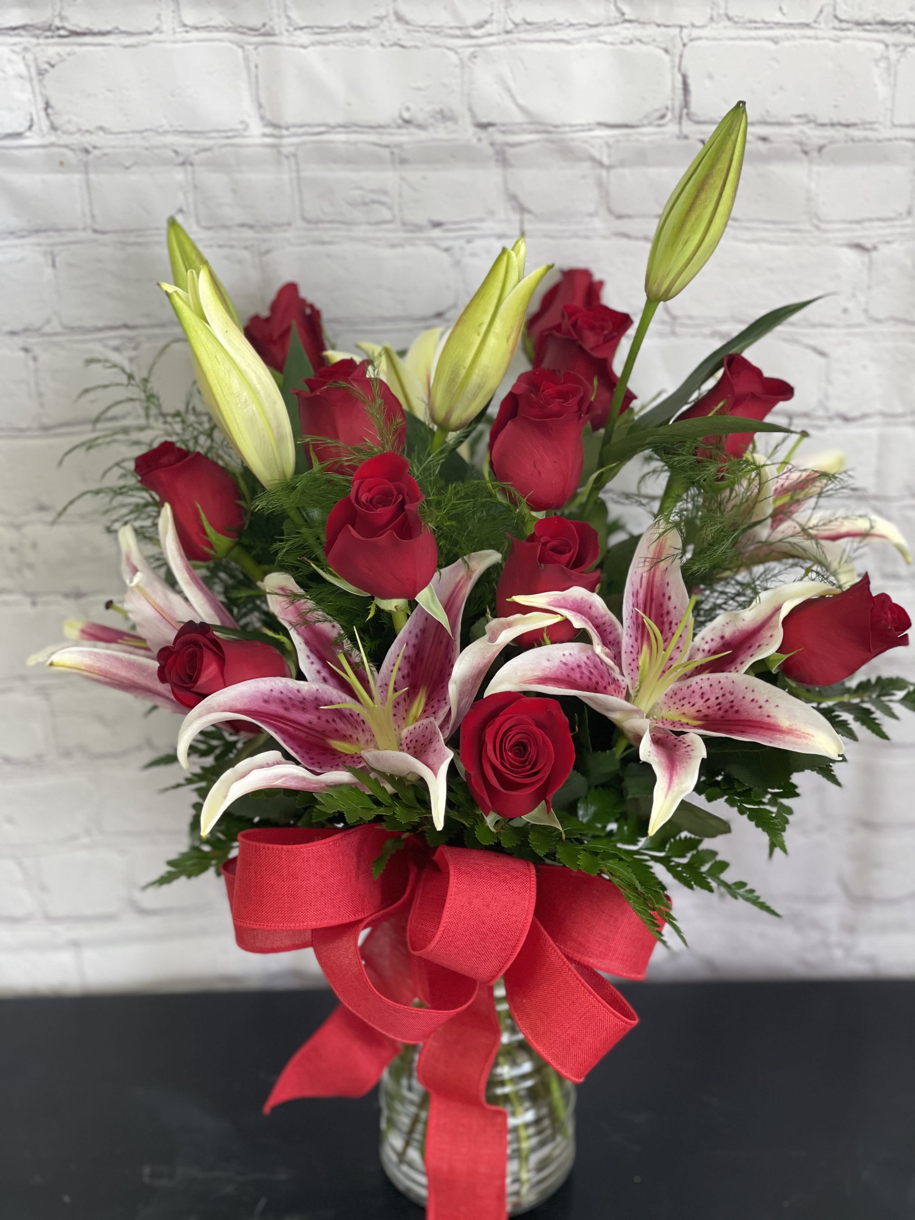 Roses and lilies - Dozen red long stem roses mixed with stargazer lilies and greenery arranged in a glass vase. 