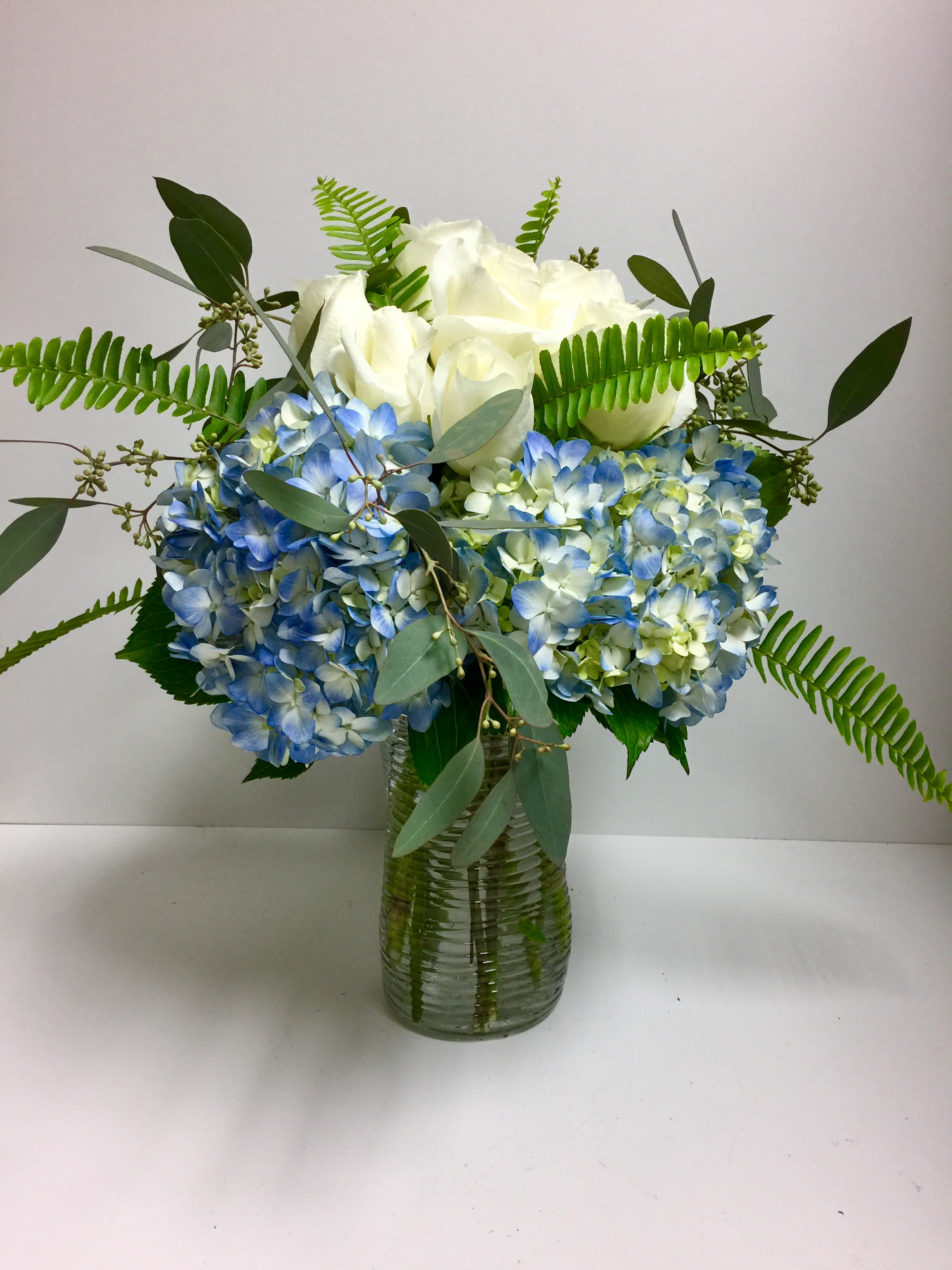 White and Blue Just for You - White roses, blue hydrangeas, seeded eucalyptus and fern carefully arranged in a glass vase that is suitable for any occasion.