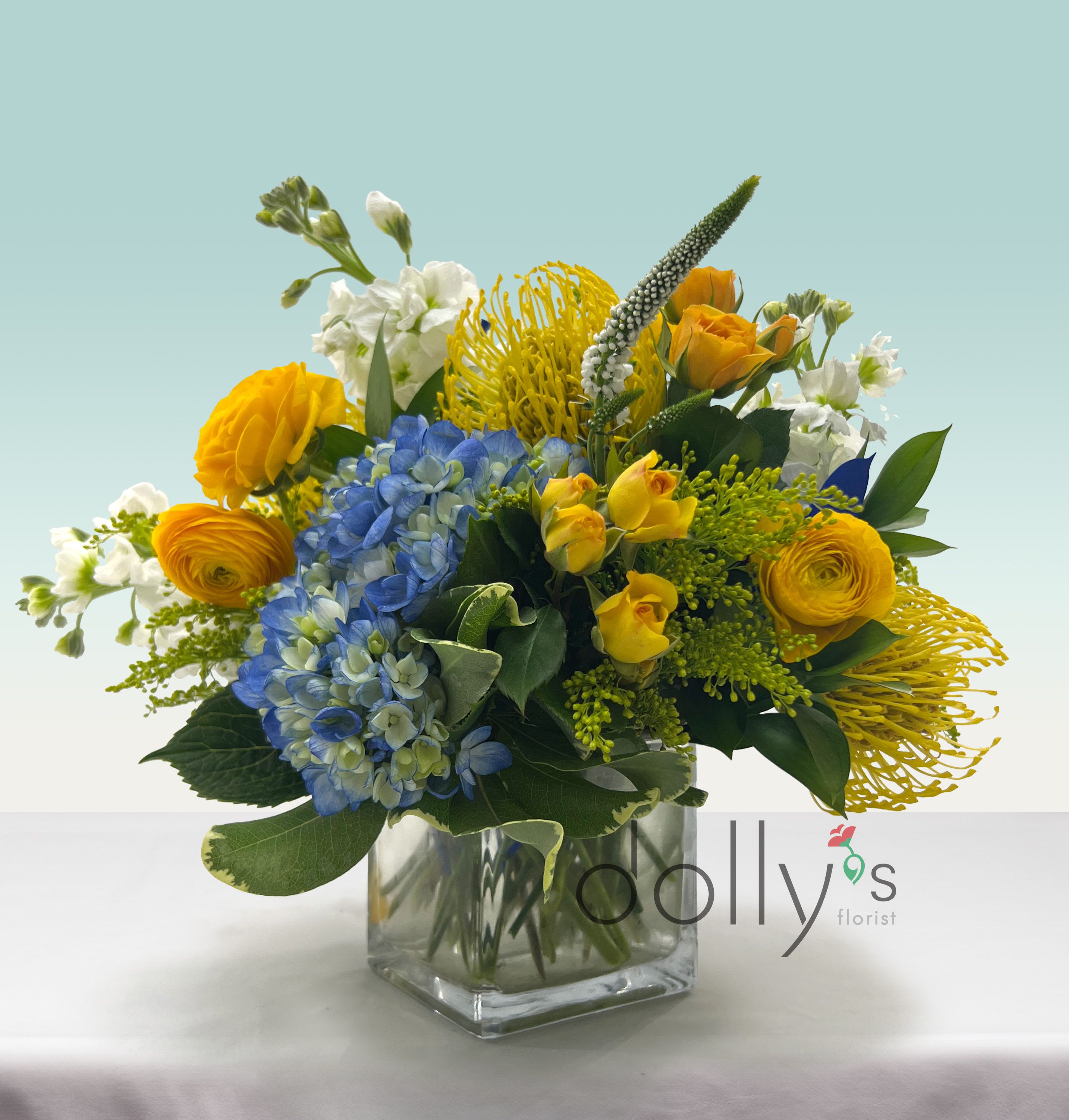 Cheerful - Bring in some cheer with this combinations of yellow protea, spray roses, and blue hydrangeas.